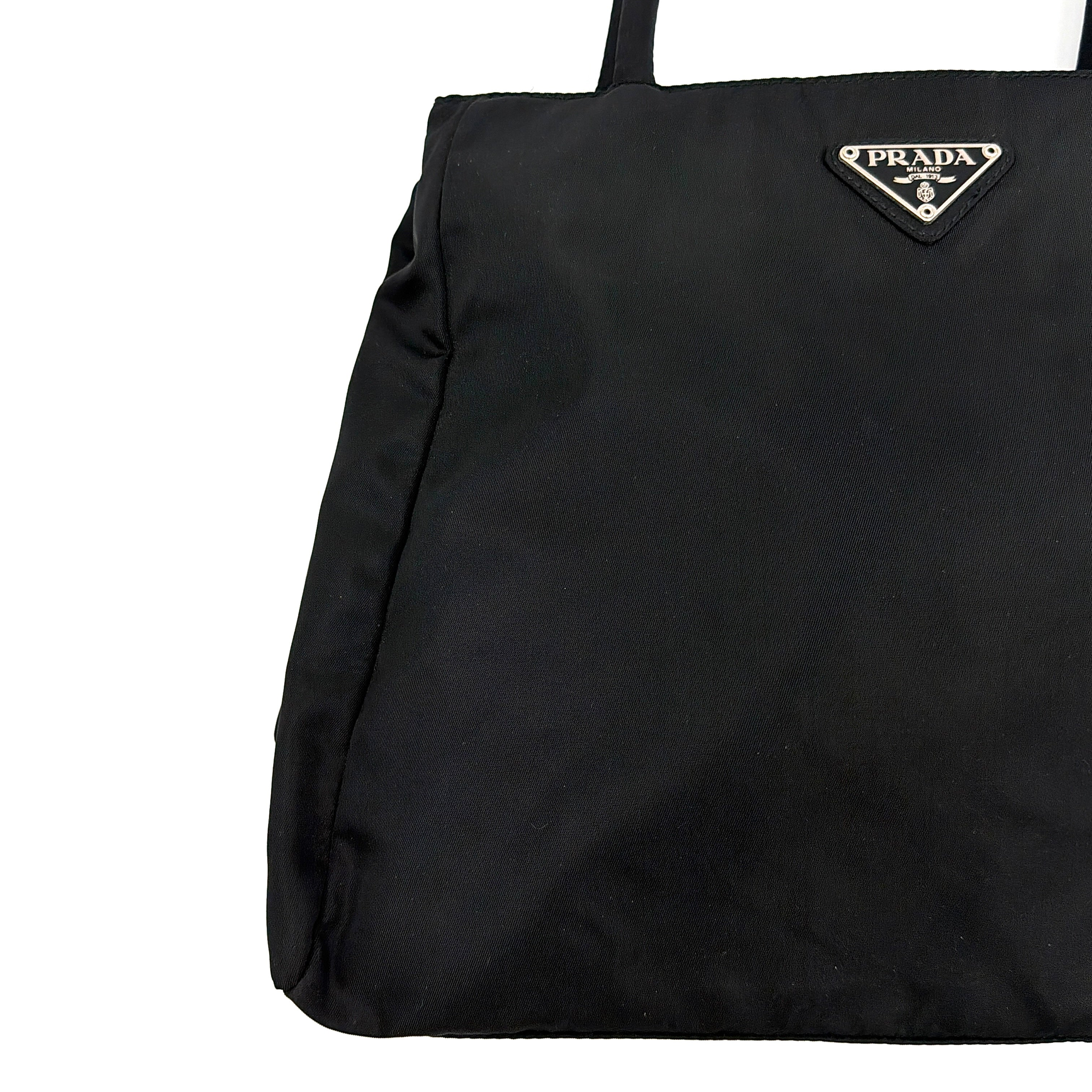 Prada Tessuto Nylon City Tote Bag in black with a structured silhouette, dual rolled handles, and a prominent Prada triangle logo plaque.