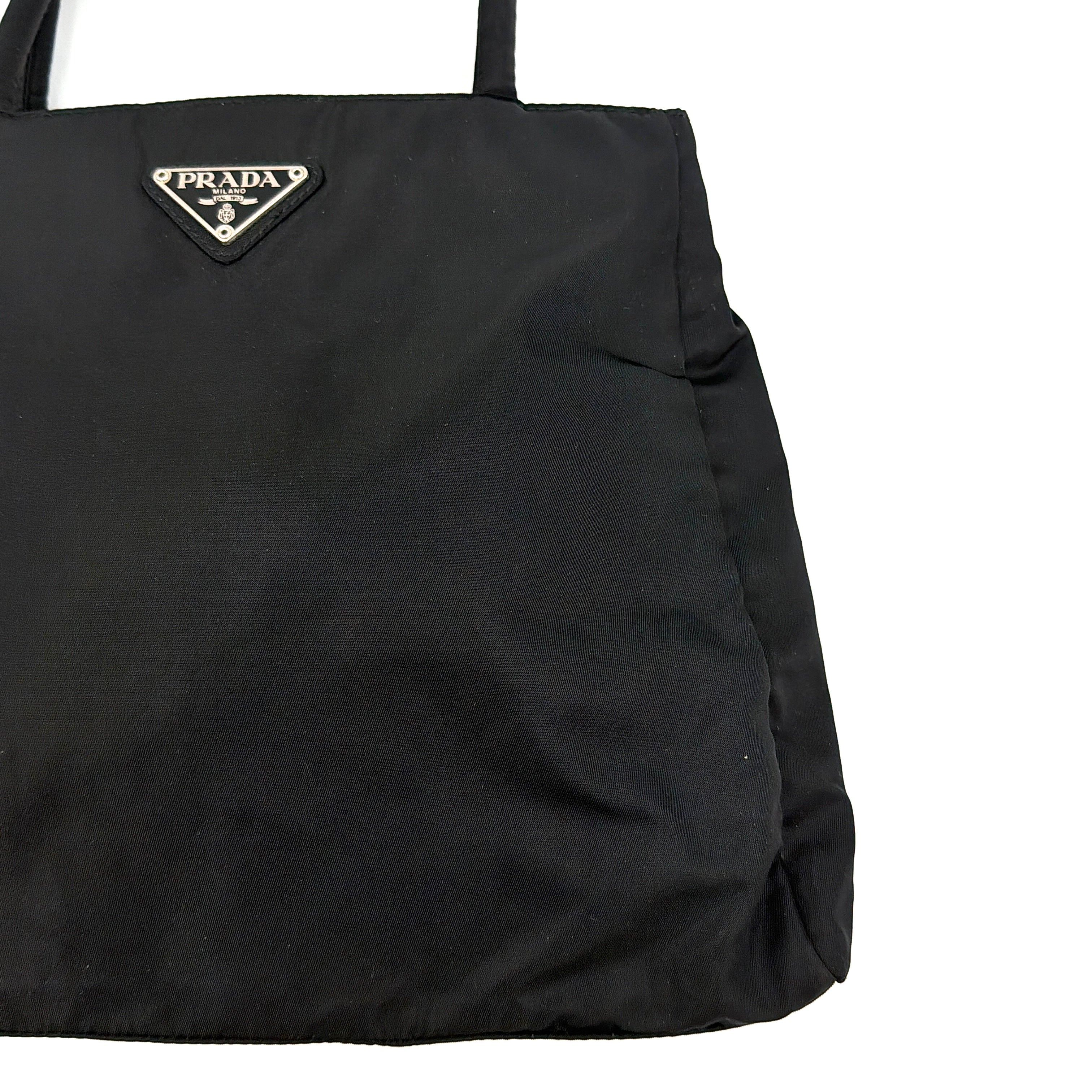 Prada Tessuto Nylon City Tote Bag in black with a structured silhouette, dual rolled handles, and a prominent Prada triangle logo plaque.