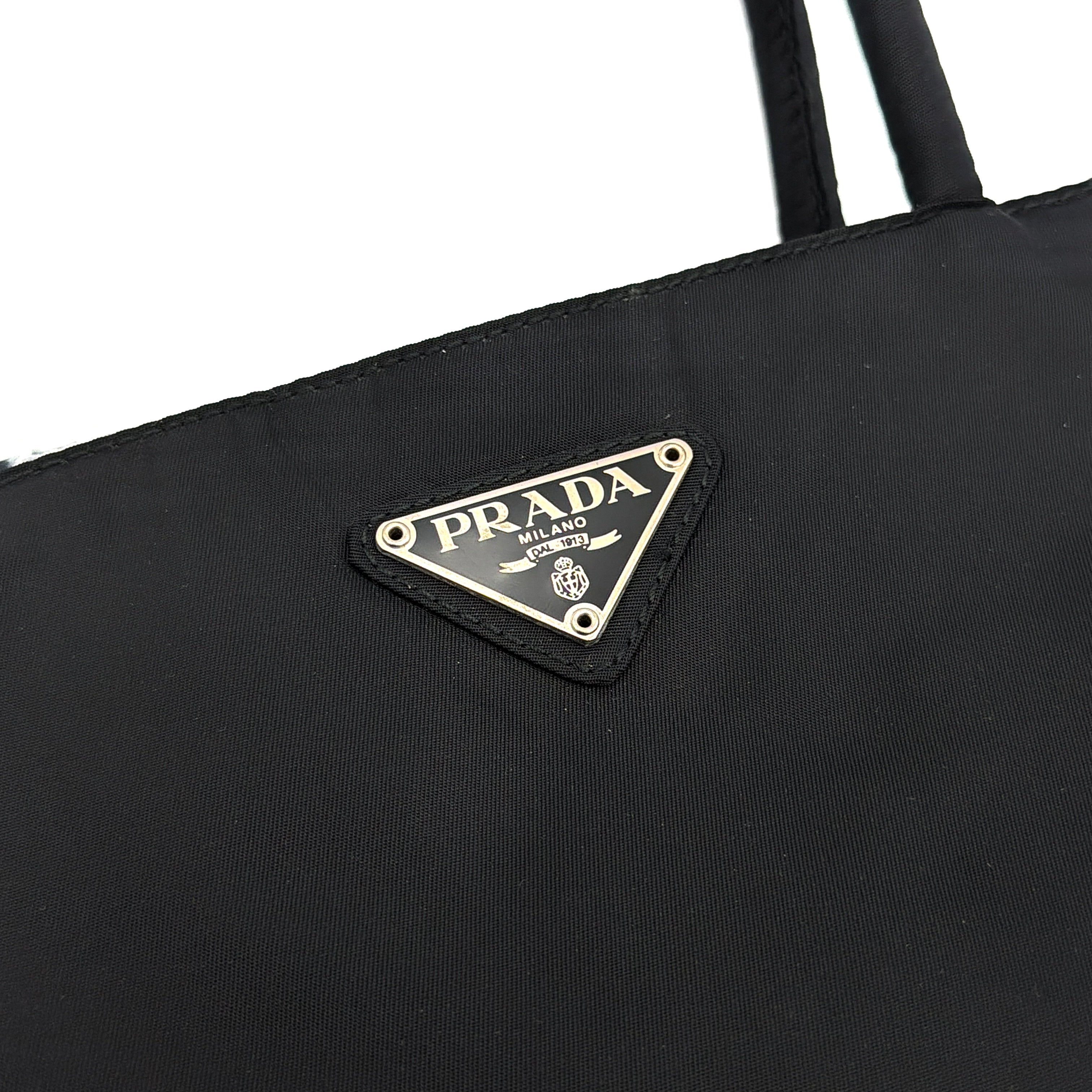 Prada Tessuto Nylon City Tote Bag in black with a structured silhouette, dual rolled handles, and a prominent Prada triangle logo plaque.