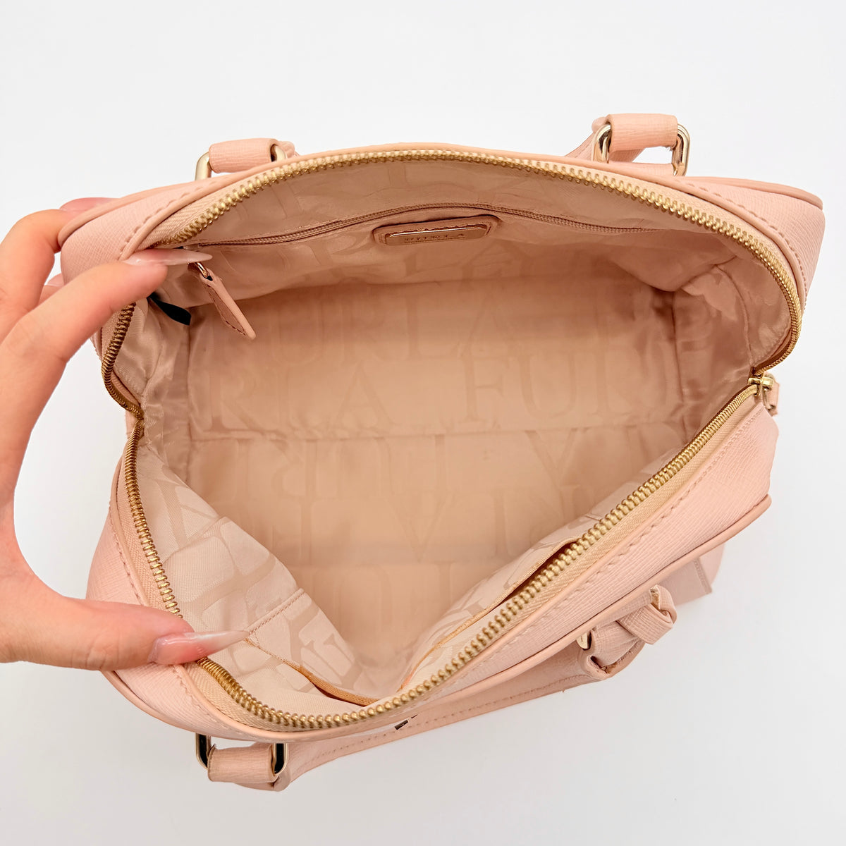 Furla Elena 2Way Saffiano leather satchel in beige with gold-tone hardware and removable strap, displayed on Furla-branded dust bag.