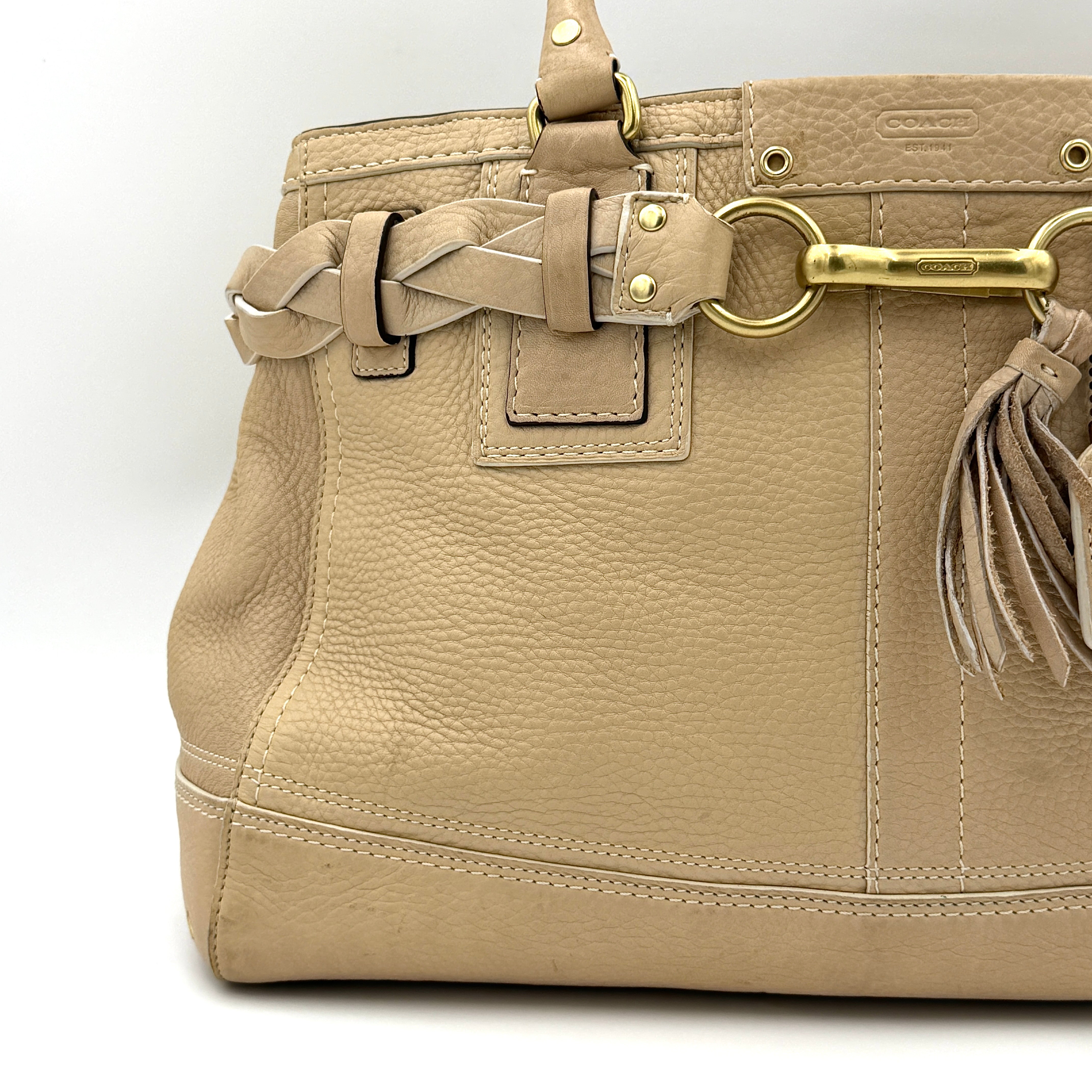 Coach beige Hampton Carryall Shoulder Bag with braided leather details, gold hardware, and tassel accent, displayed front-facing.