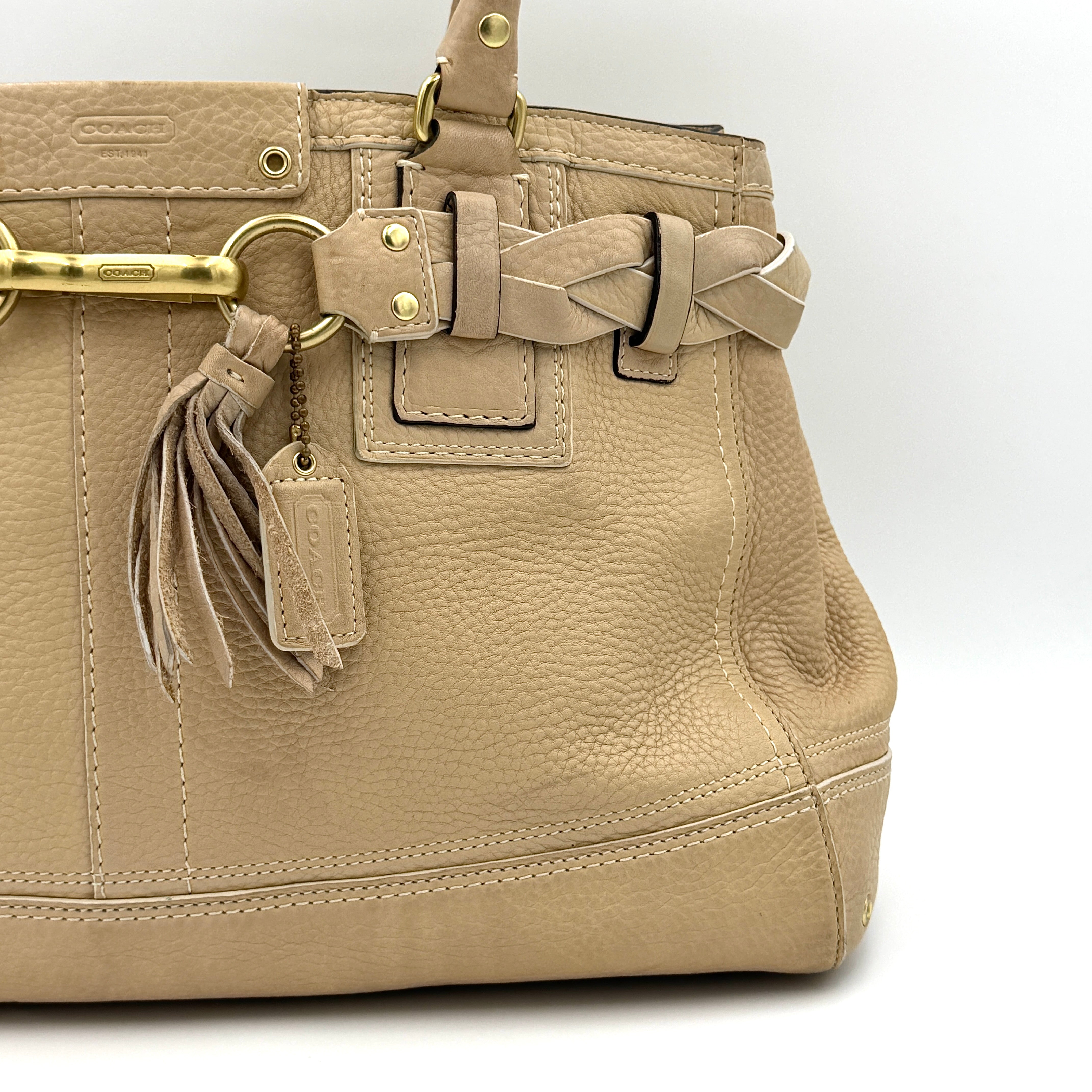 Coach beige Hampton Carryall Shoulder Bag with braided leather details, gold hardware, and tassel accent, displayed front-facing.