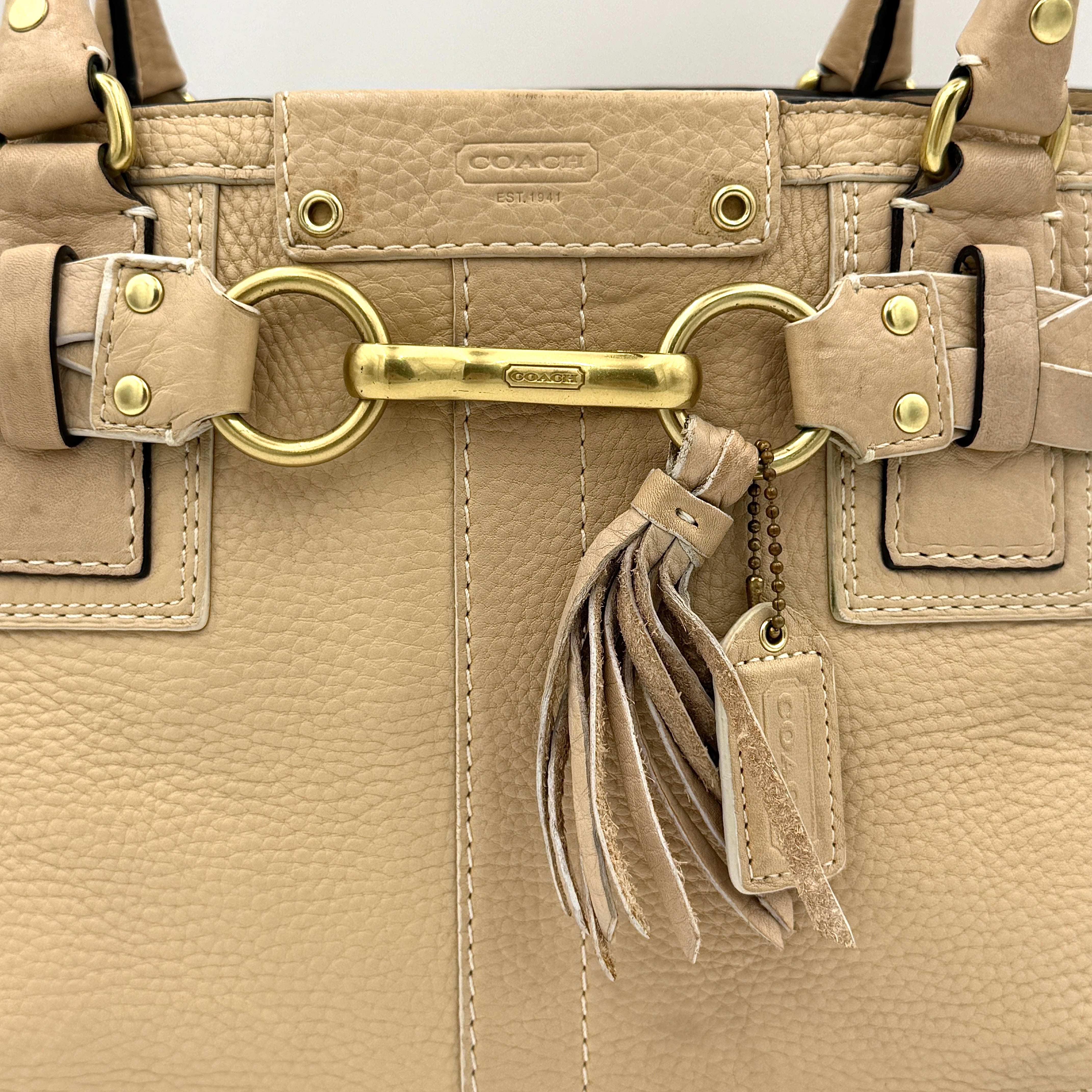Coach beige Hampton Carryall Shoulder Bag with braided leather details, gold hardware, and tassel accent, displayed front-facing.