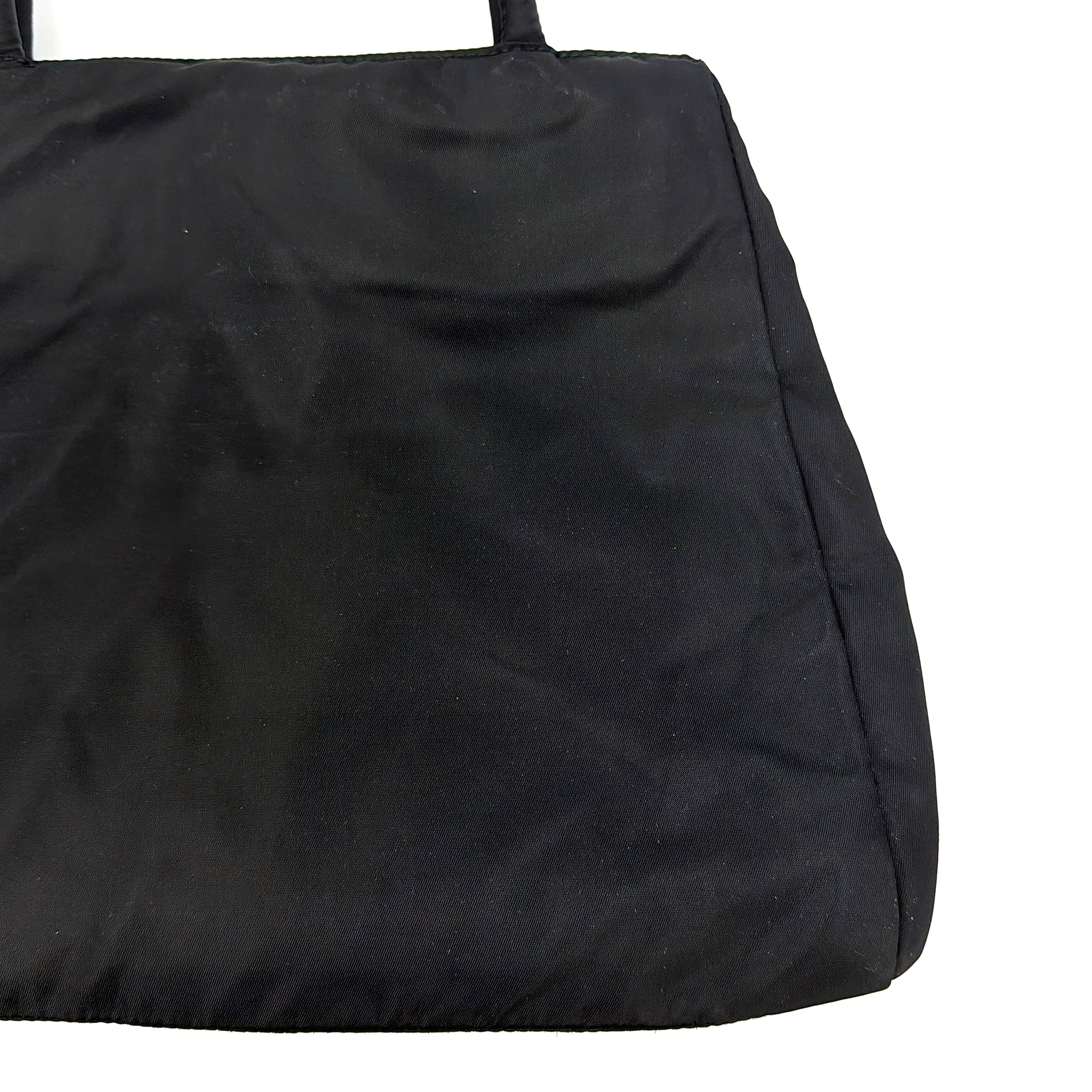 Prada Tessuto Nylon City Tote Bag in black with a structured silhouette, dual rolled handles, and a prominent Prada triangle logo plaque.