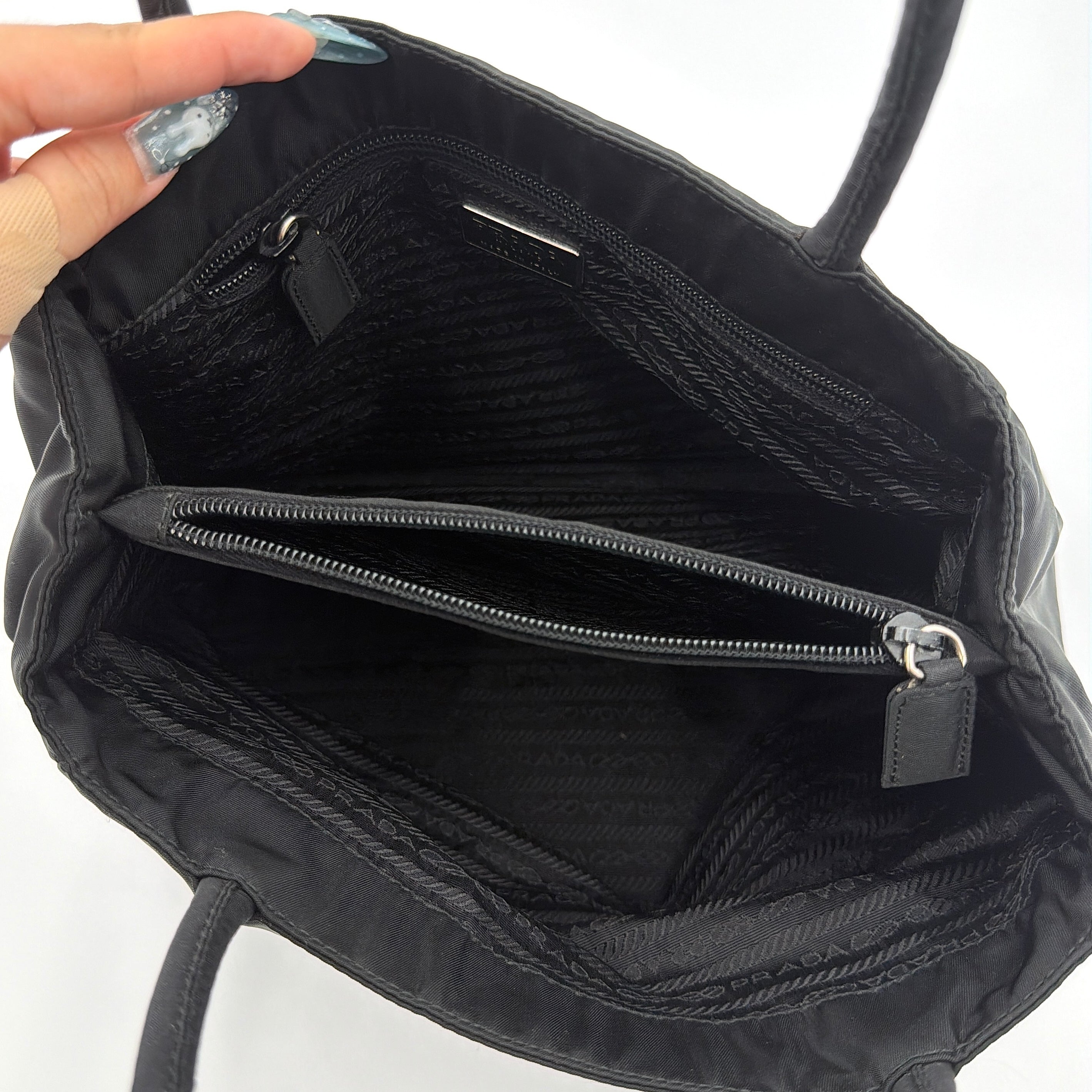 Prada Tessuto Nylon City Tote Bag in black with a structured silhouette, dual rolled handles, and a prominent Prada triangle logo plaque.