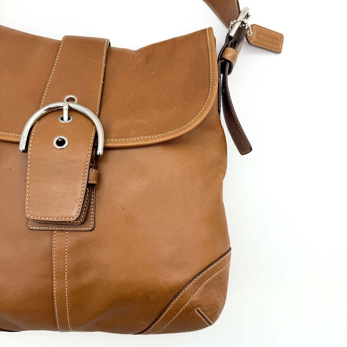 Coach Soho Buckle Flap Crossbody Bag in brown leather with buckle flap and adjustable strap, displayed on white background.
