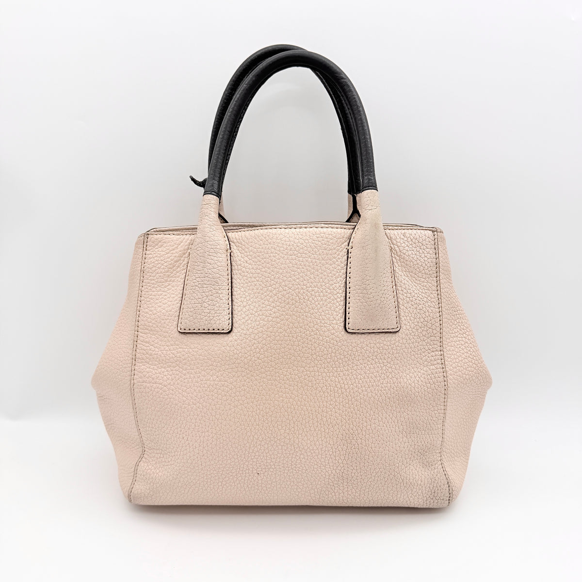 Kate Spade New York beige leather satchel with black handles, gold medallion, and grained texture against a white background.