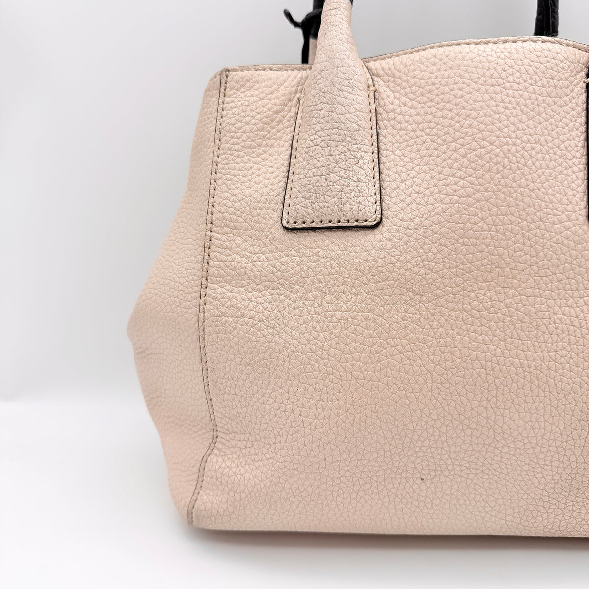 Kate Spade New York beige leather satchel with black handles, gold medallion, and grained texture against a white background.