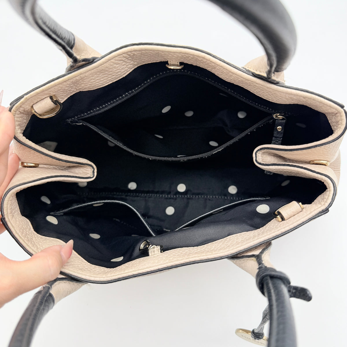 Kate Spade New York beige leather satchel with black handles, gold medallion, and grained texture against a white background.