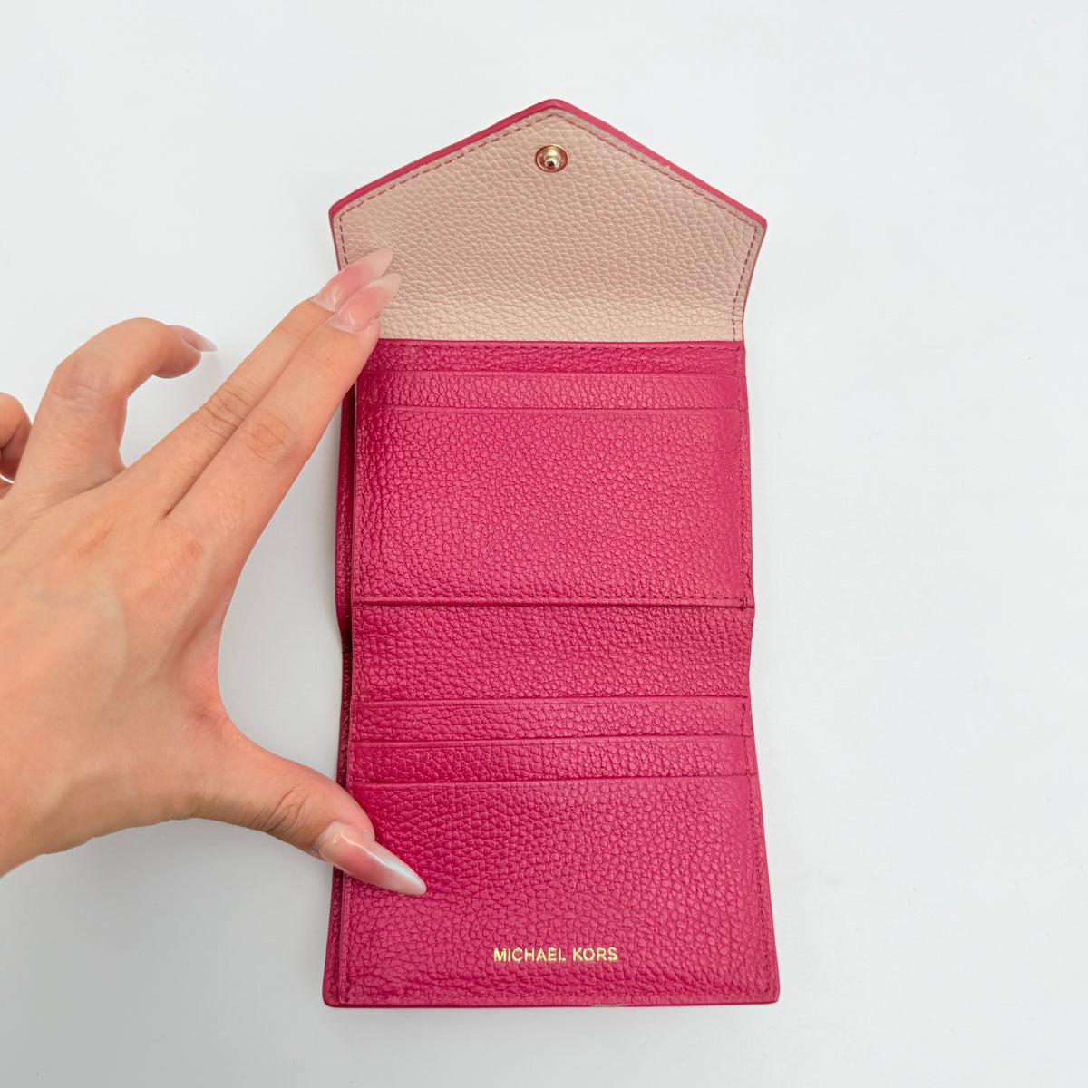 Michael Kors pink leather envelope trifold wallet with gold MK logo, shown closed on a white background.