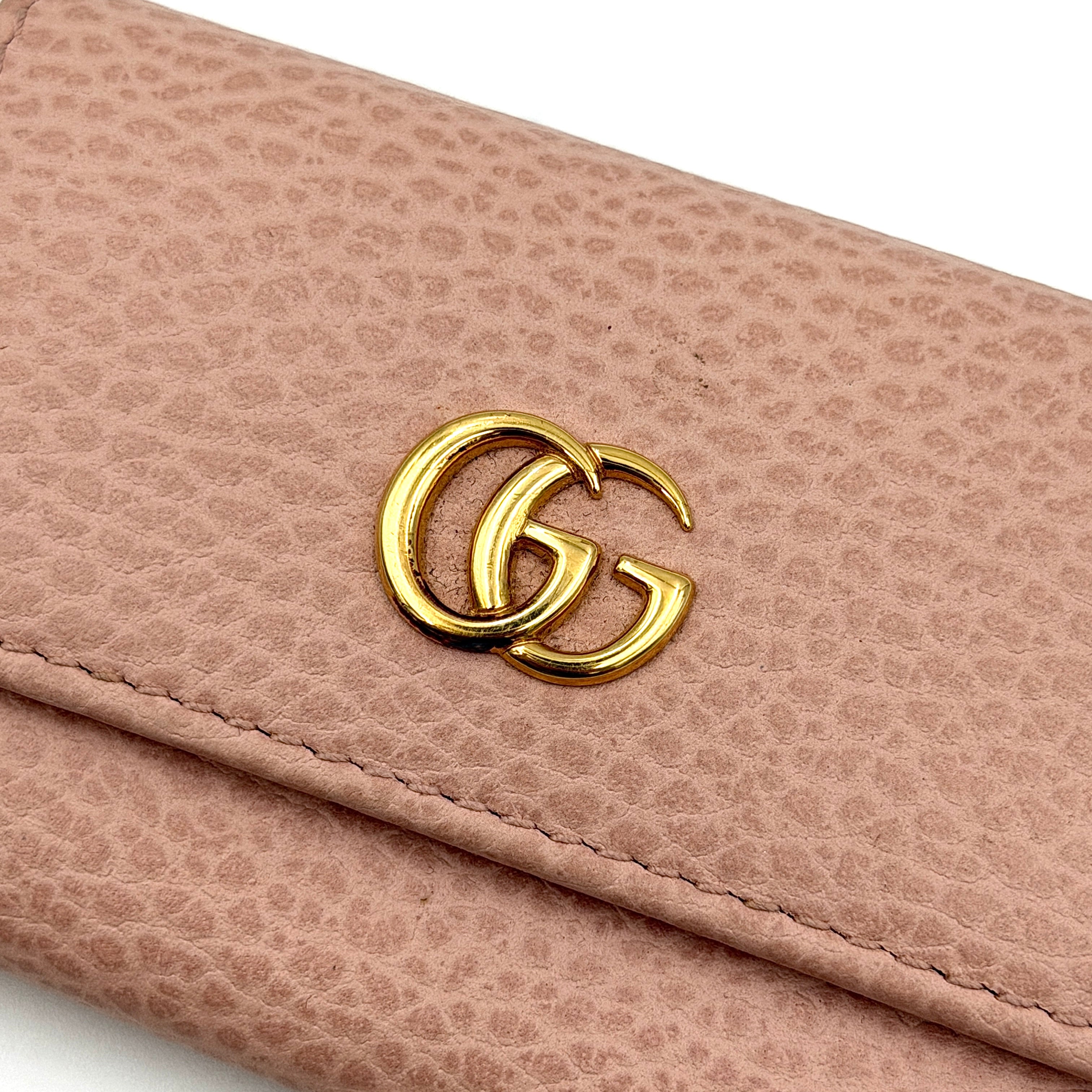 Gucci GG Marmont pink leather key case with gold GG emblem and grained texture, presented in a structured trifold shape.