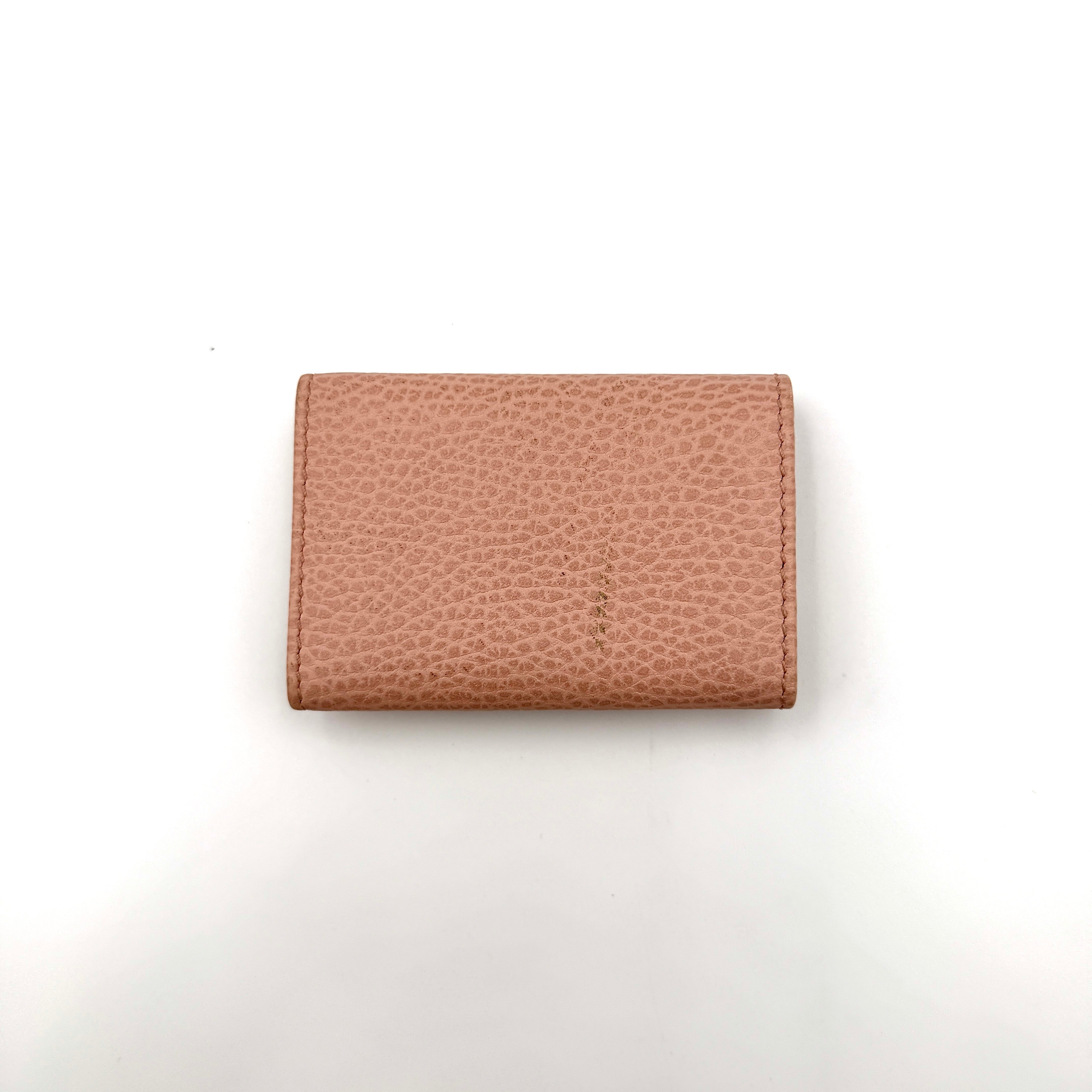 Gucci GG Marmont pink leather key case with gold GG emblem and grained texture, presented in a structured trifold shape.