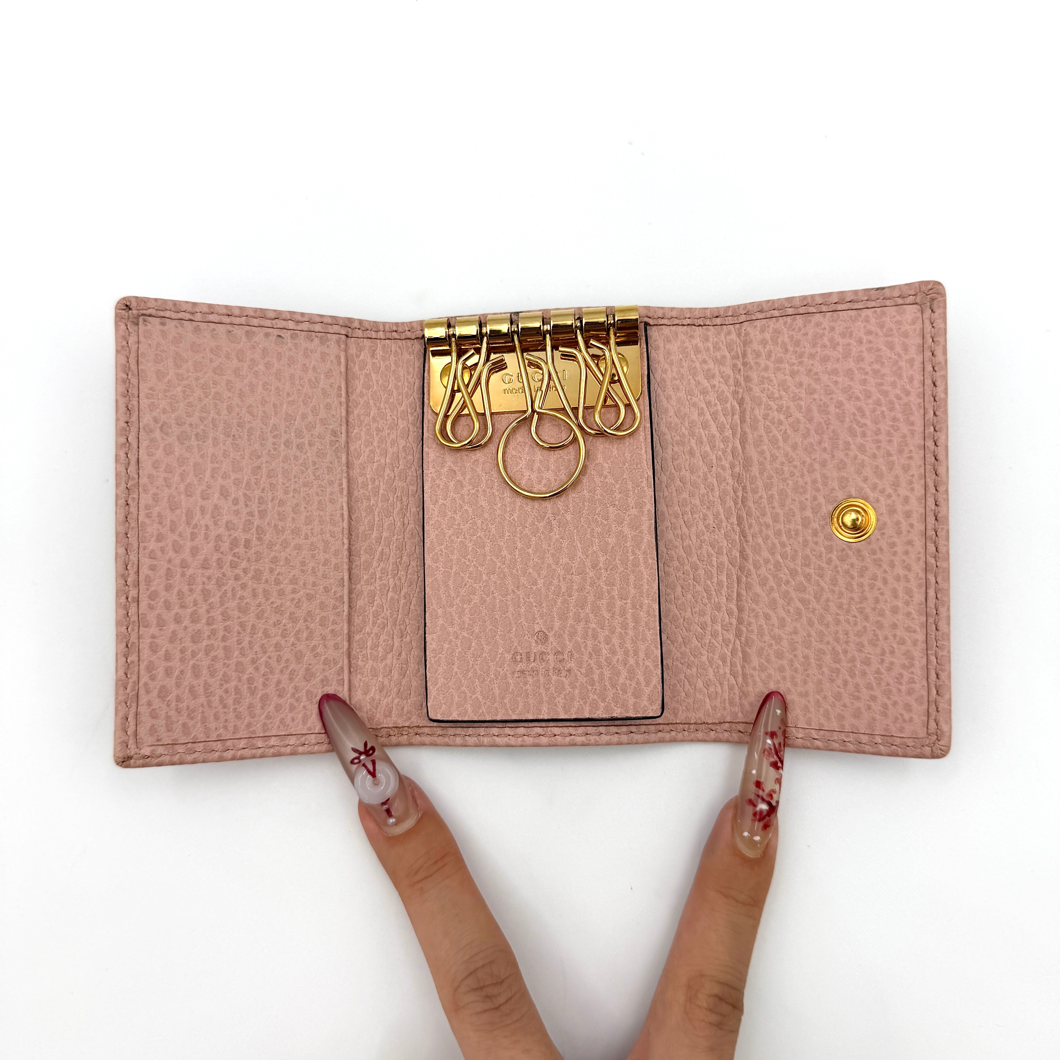 Gucci GG Marmont pink leather key case with gold GG emblem and grained texture, presented in a structured trifold shape.