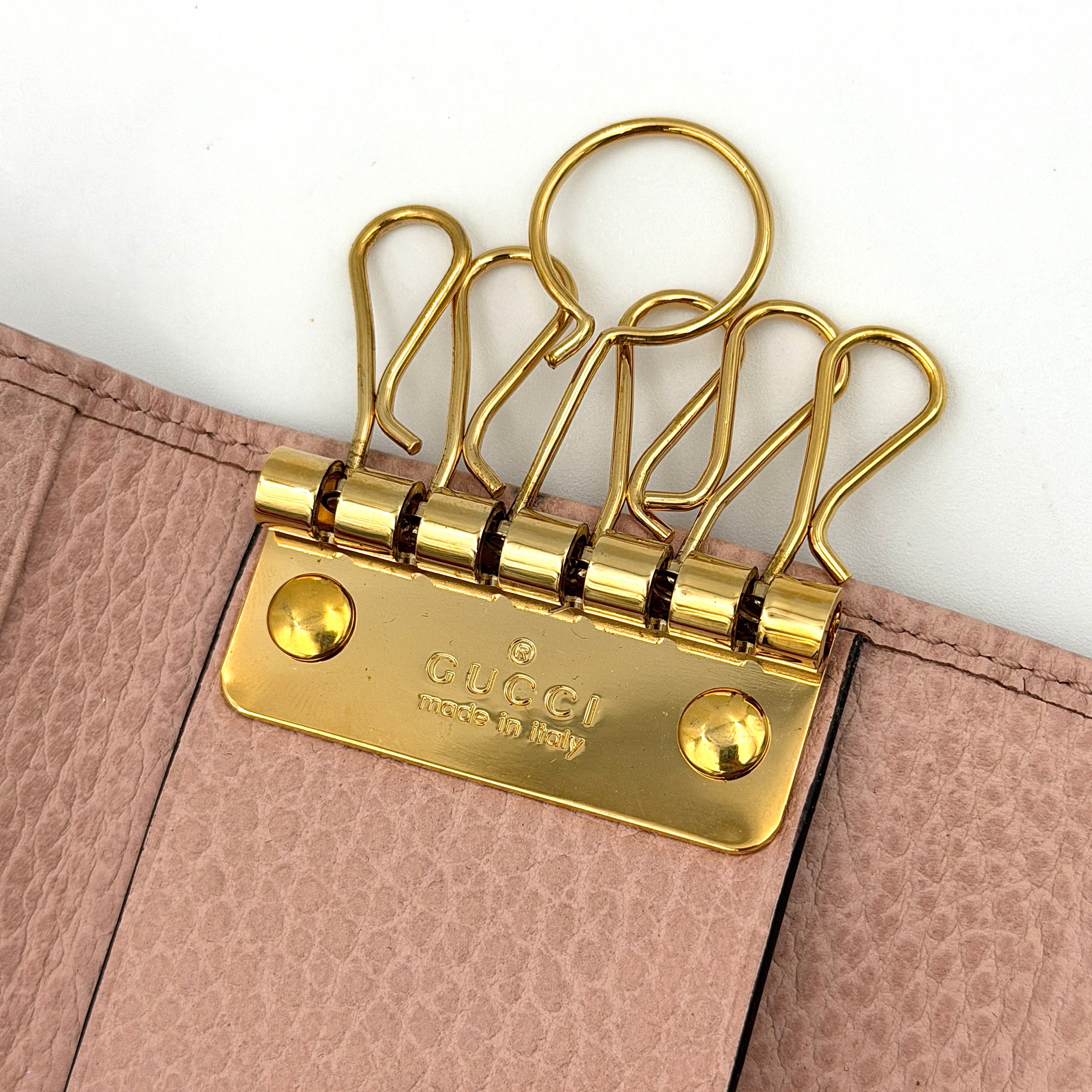 Gucci GG Marmont pink leather key case with gold GG emblem and grained texture, presented in a structured trifold shape.