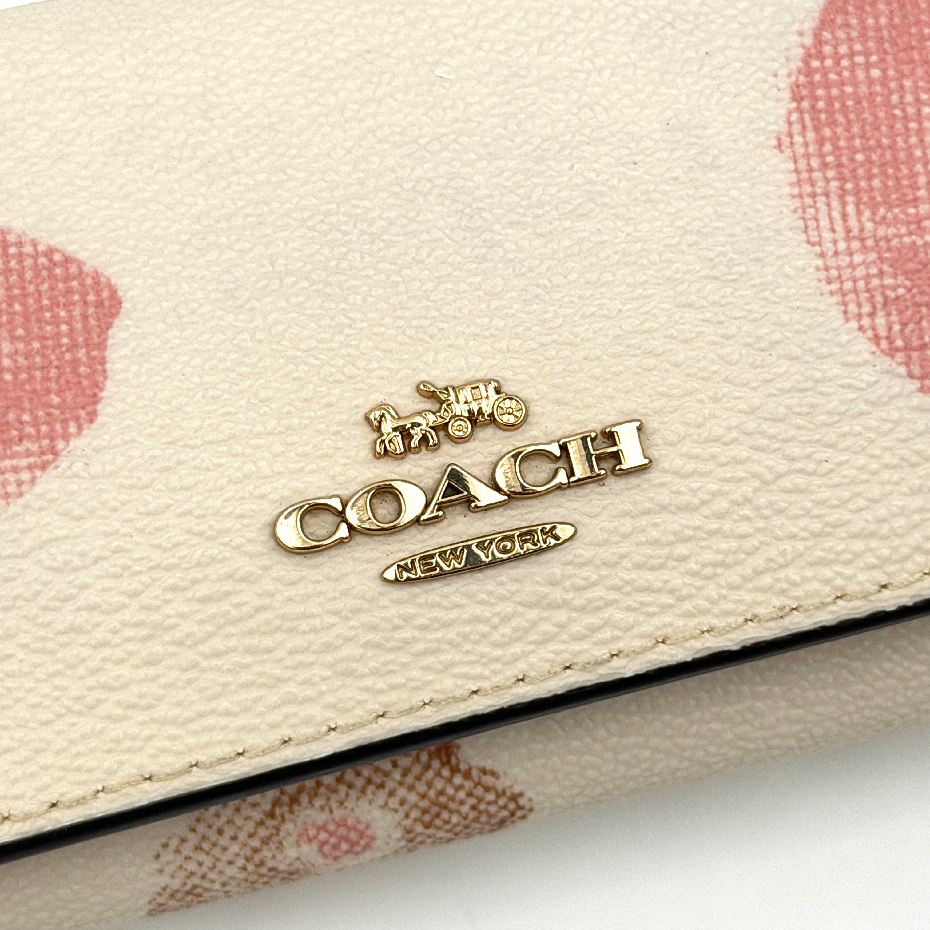 Coach floral print key case in cream with pink and brown blossom accents, gold hardware and structured silhouette.