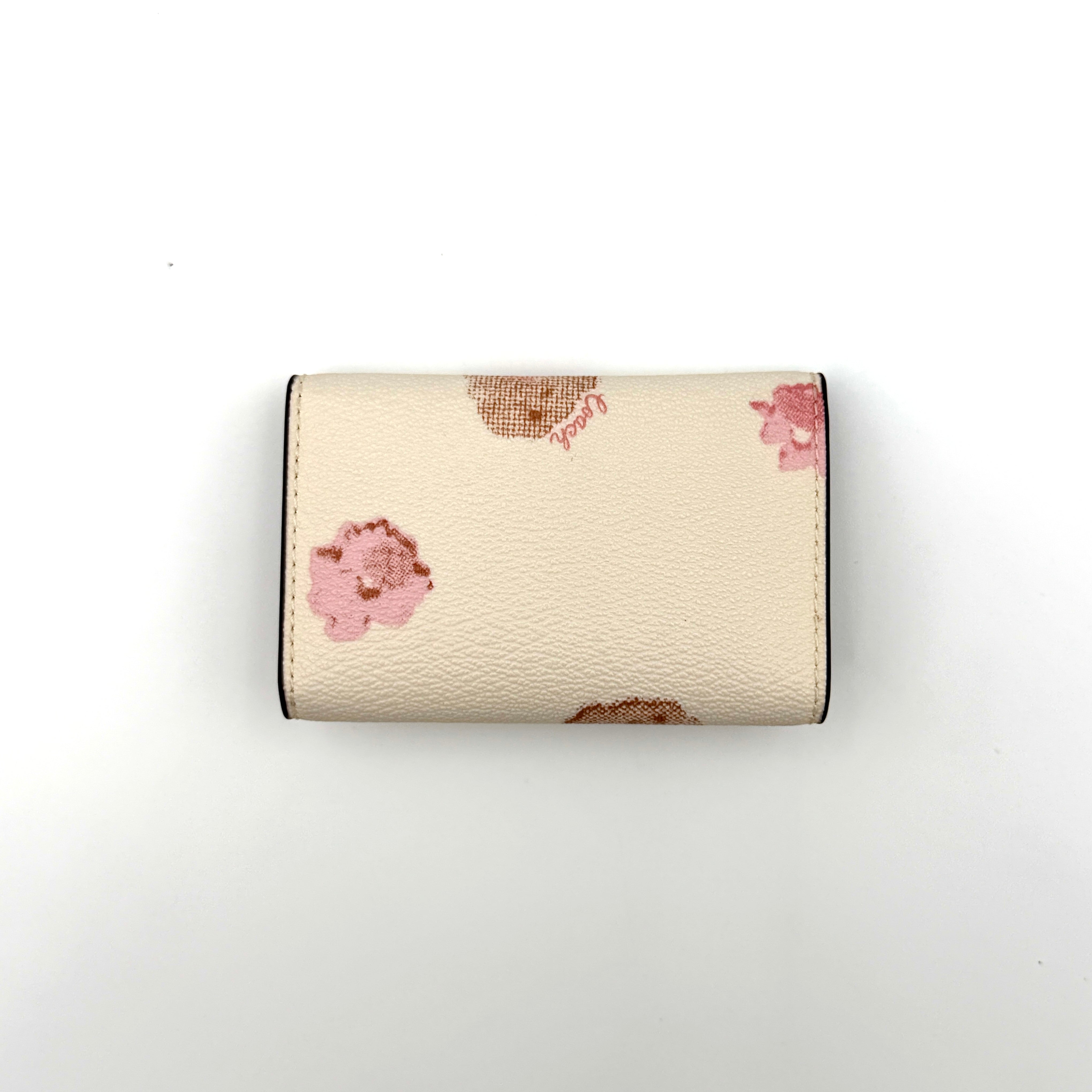 Coach floral print key case in cream with pink and brown blossom accents, gold hardware and structured silhouette.