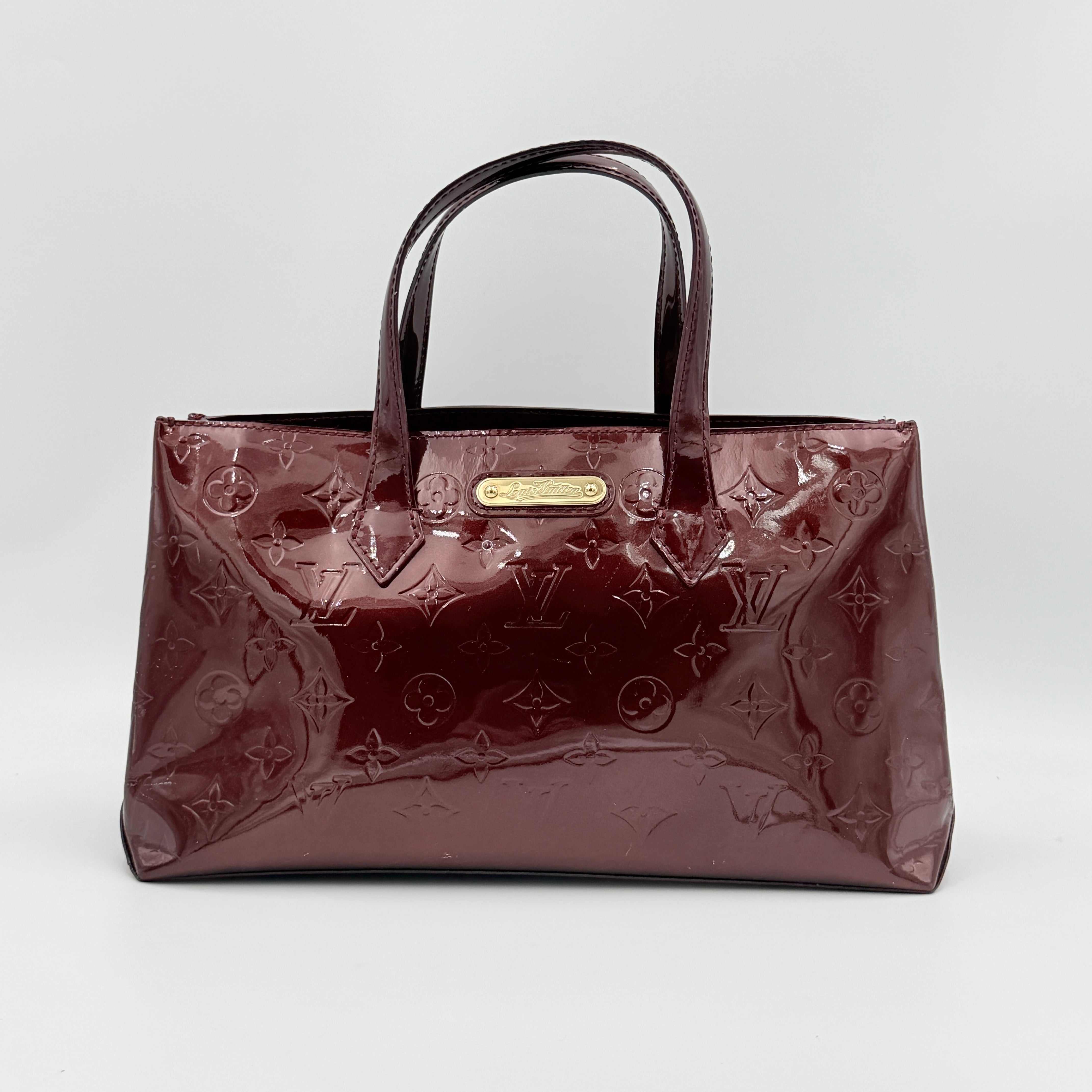 Louis Vuitton Wilshire PM Monogram Vernis bag in glossy deep red with gold nameplate and embossed monogram, displayed against a clean background.