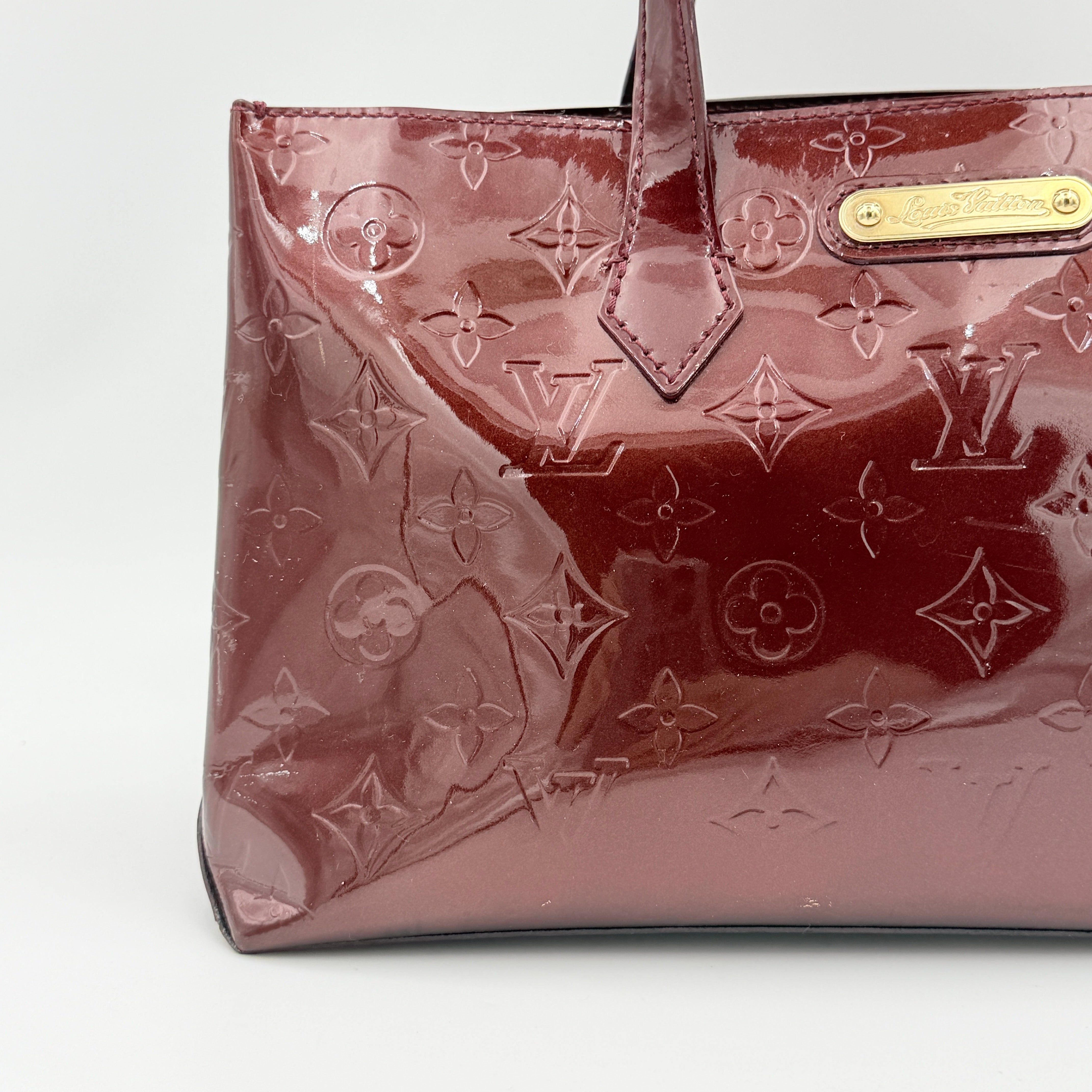 Louis Vuitton Wilshire PM Monogram Vernis bag in glossy deep red with gold nameplate and embossed monogram, displayed against a clean background.