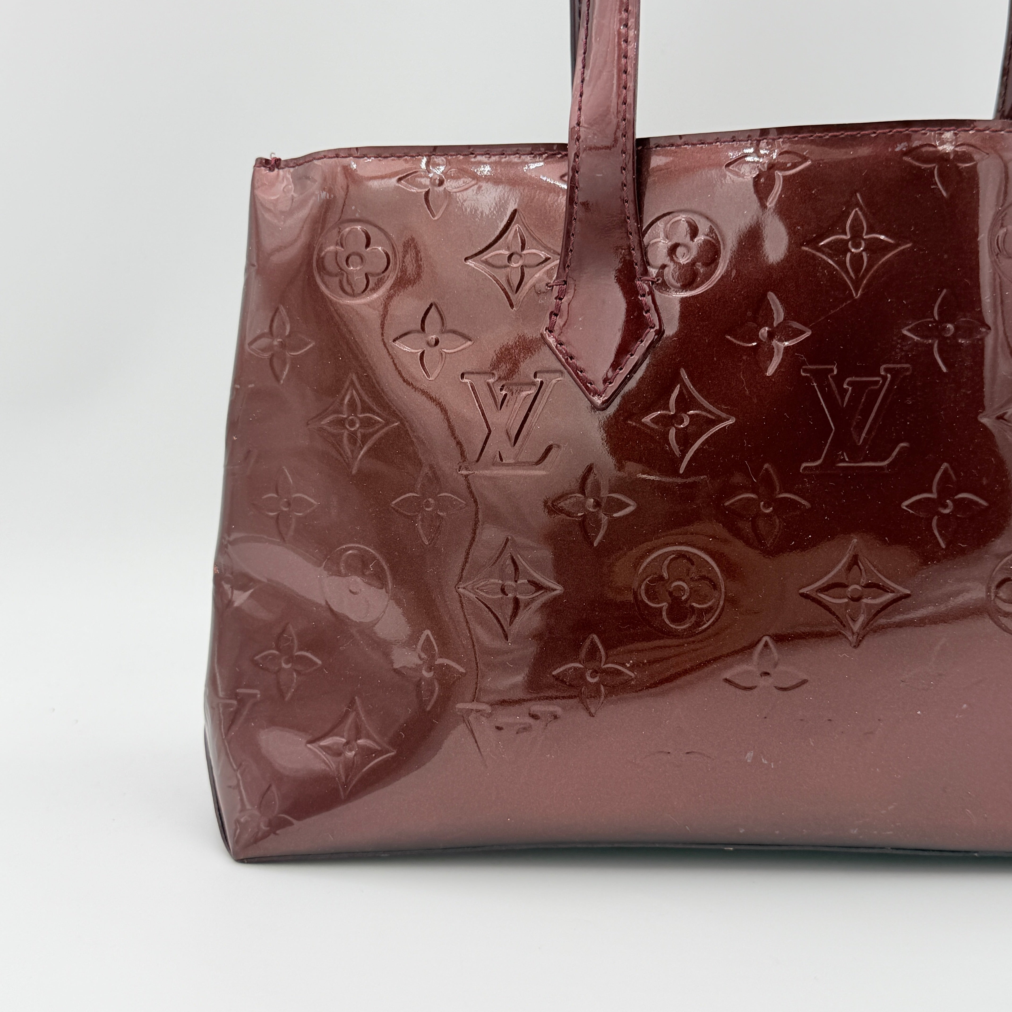 Louis Vuitton Wilshire PM Monogram Vernis bag in glossy deep red with gold nameplate and embossed monogram, displayed against a clean background.