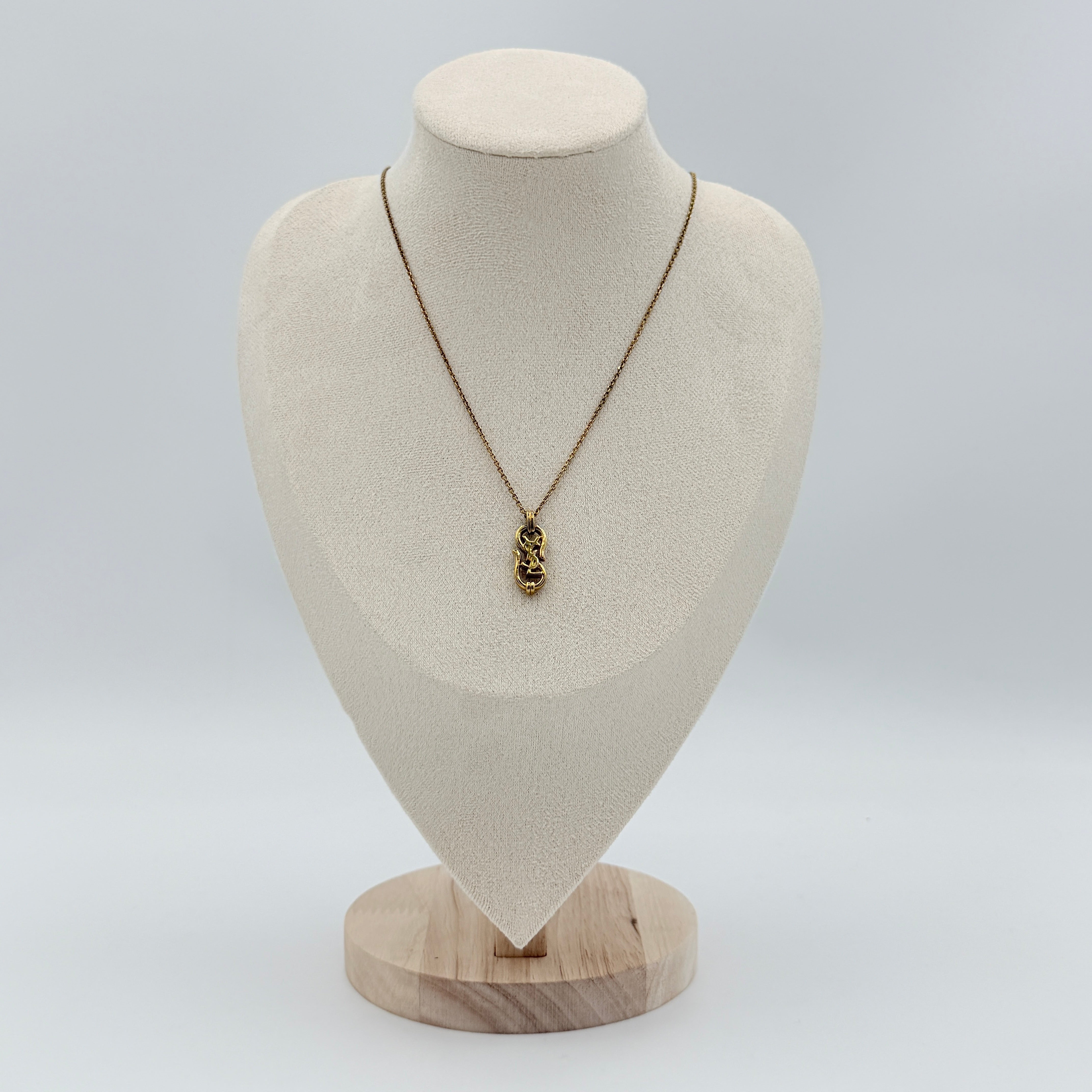 Saint Laurent Cassandre Logo Necklace in gold metal with signature YSL pendant displayed on a necklace stand.