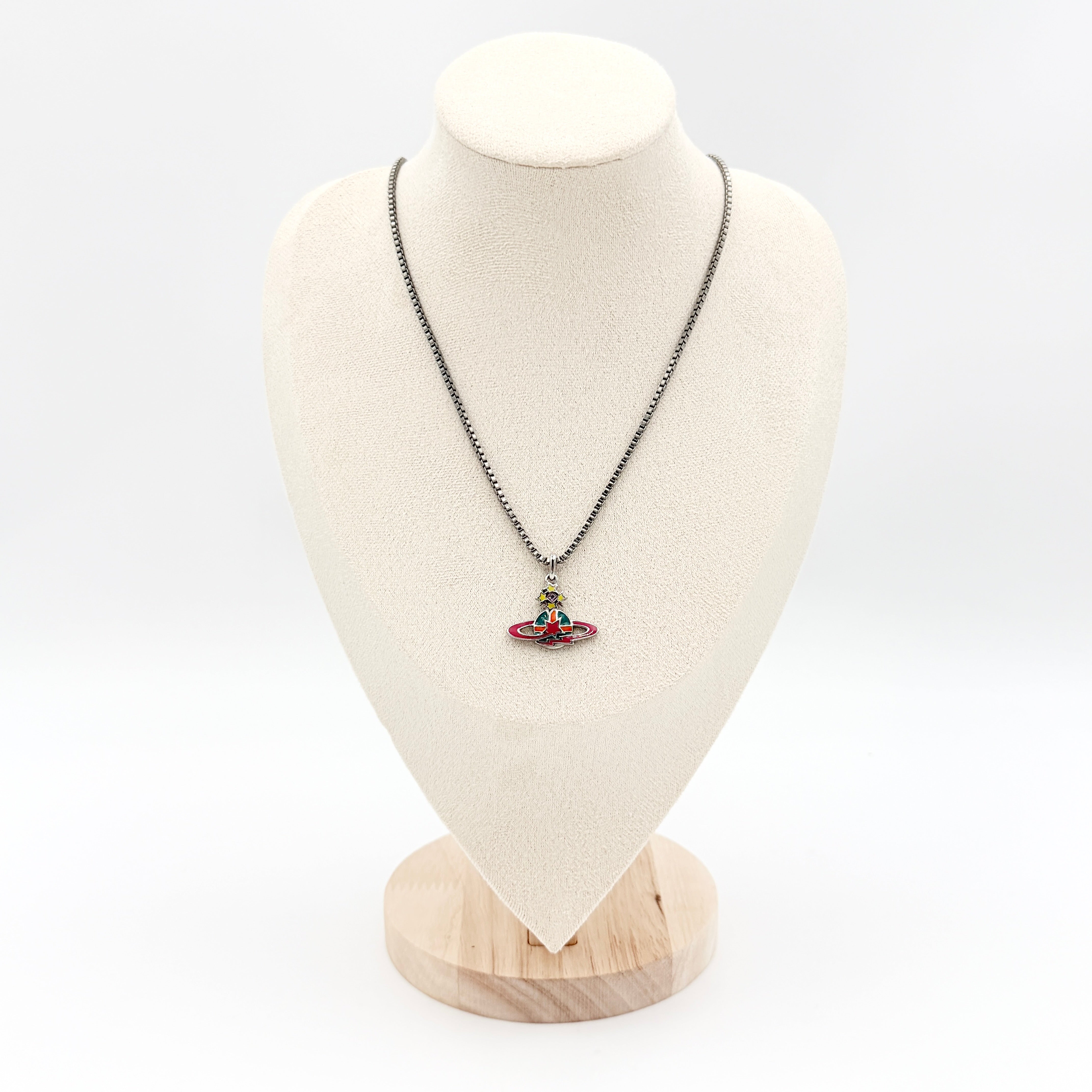 Vivienne Westwood Shooting Star Orb Necklace in silver with vibrant multi-coloured enamel details displayed on a cream jewellery stand.
