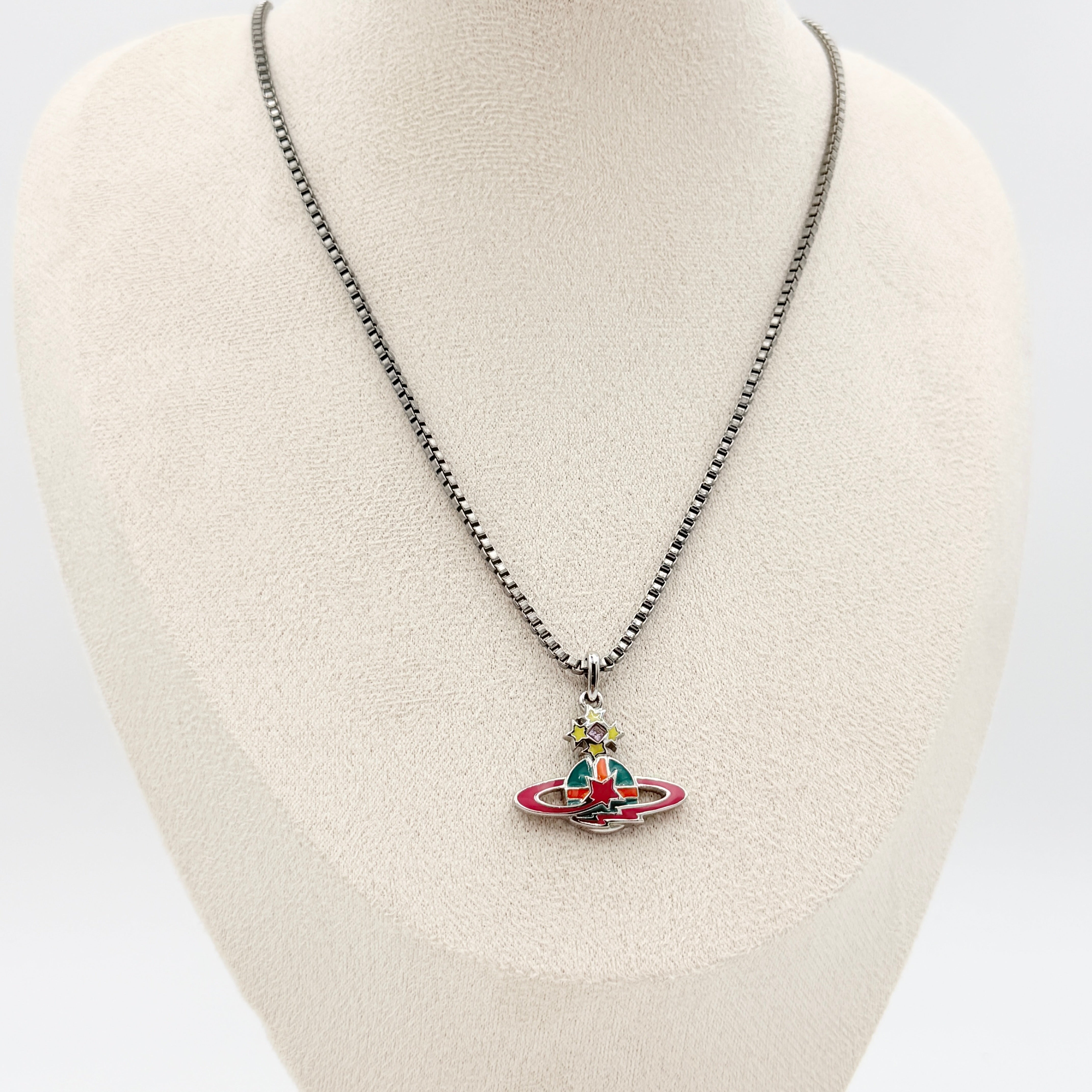 Vivienne Westwood Shooting Star Orb Necklace in silver with vibrant multi-coloured enamel details displayed on a cream jewellery stand.