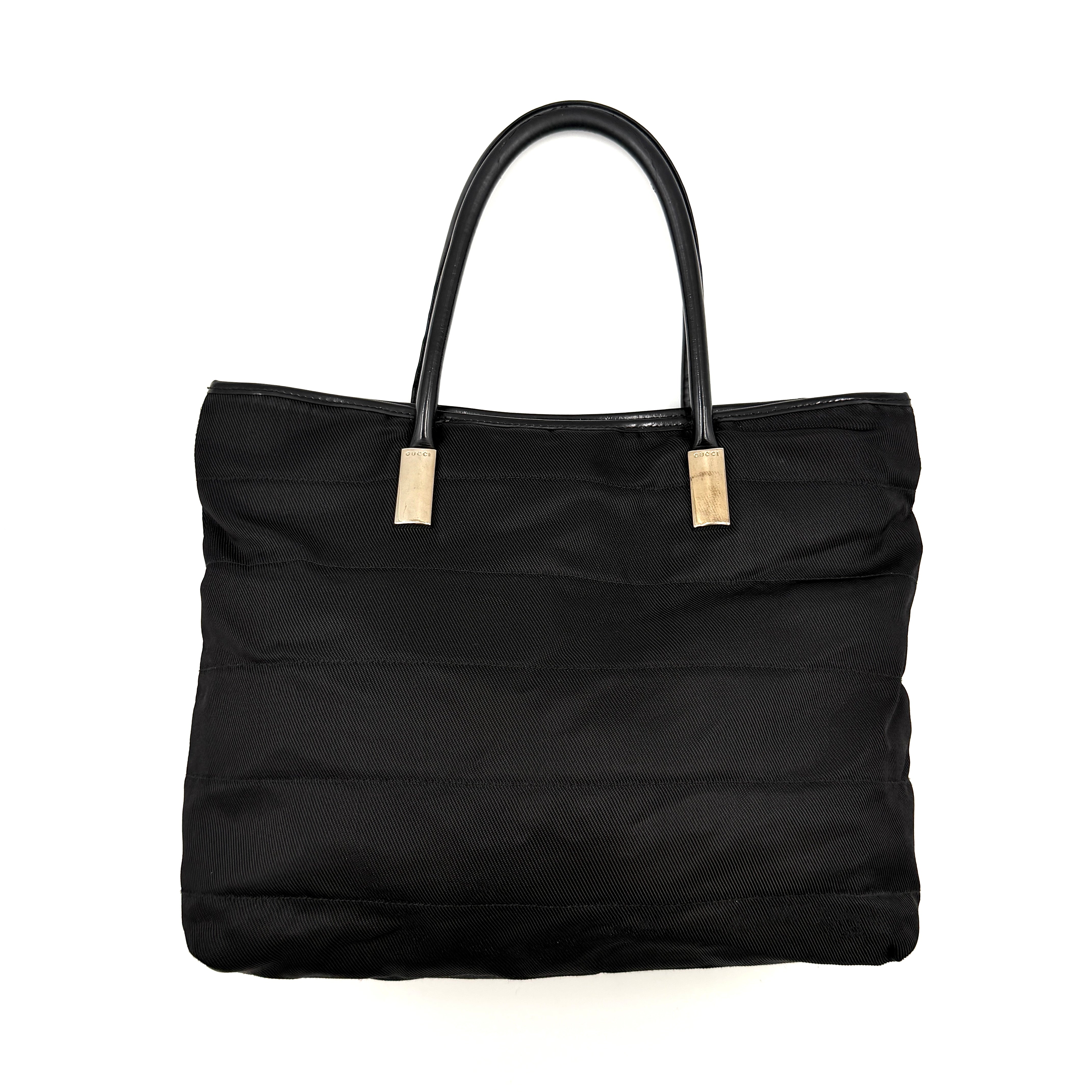 A classic black Gucci nylon tote bag with leather handles and gold-tone hardware displayed upright against a clean background.