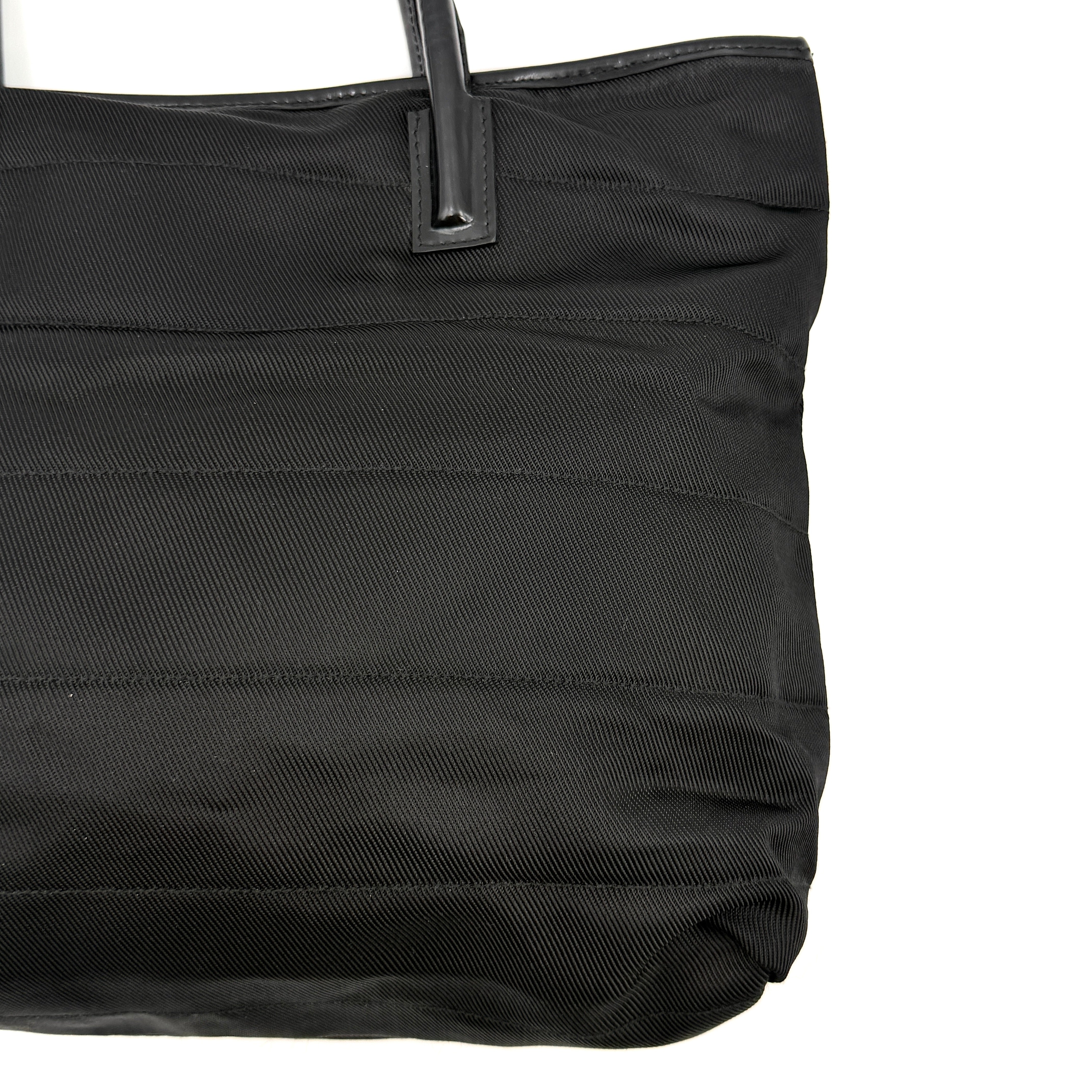 A classic black Gucci nylon tote bag with leather handles and gold-tone hardware displayed upright against a clean background.