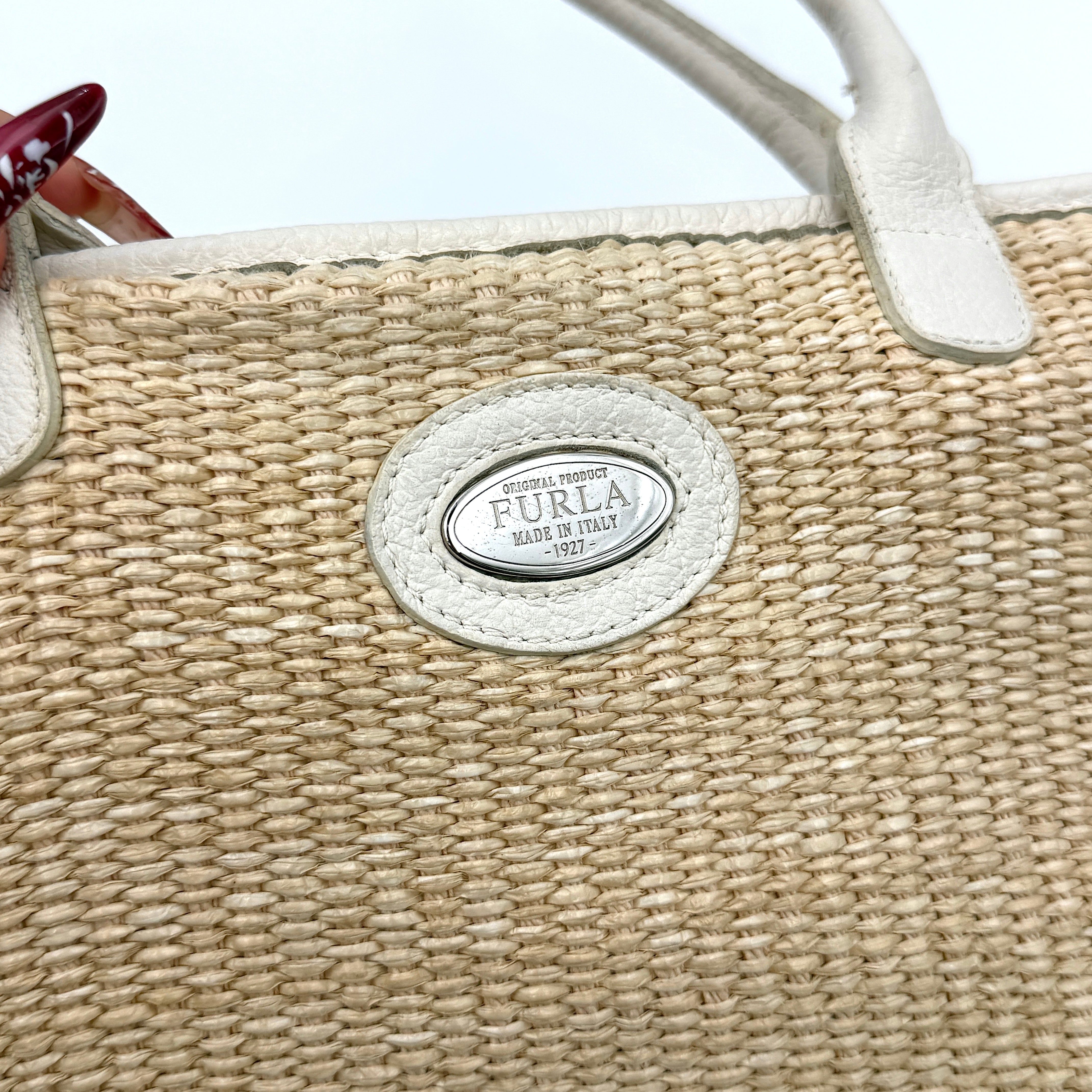 Furla beige woven straw tote bag with off-white leather handles and corners, featuring a silver oval logo plaque.