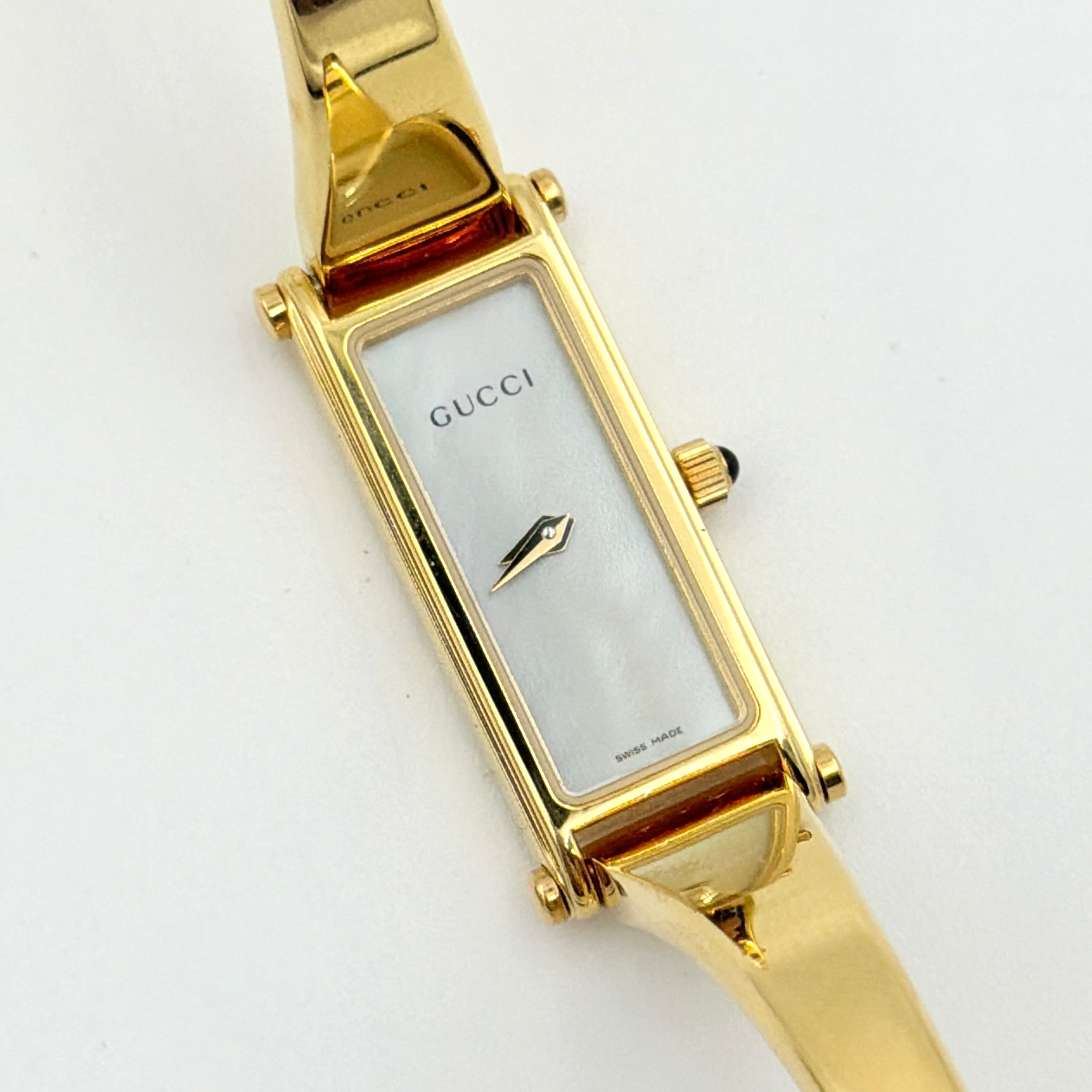 Gucci 1500L gold-tone quartz watch with white rectangular dial, displayed in box with warranty card.