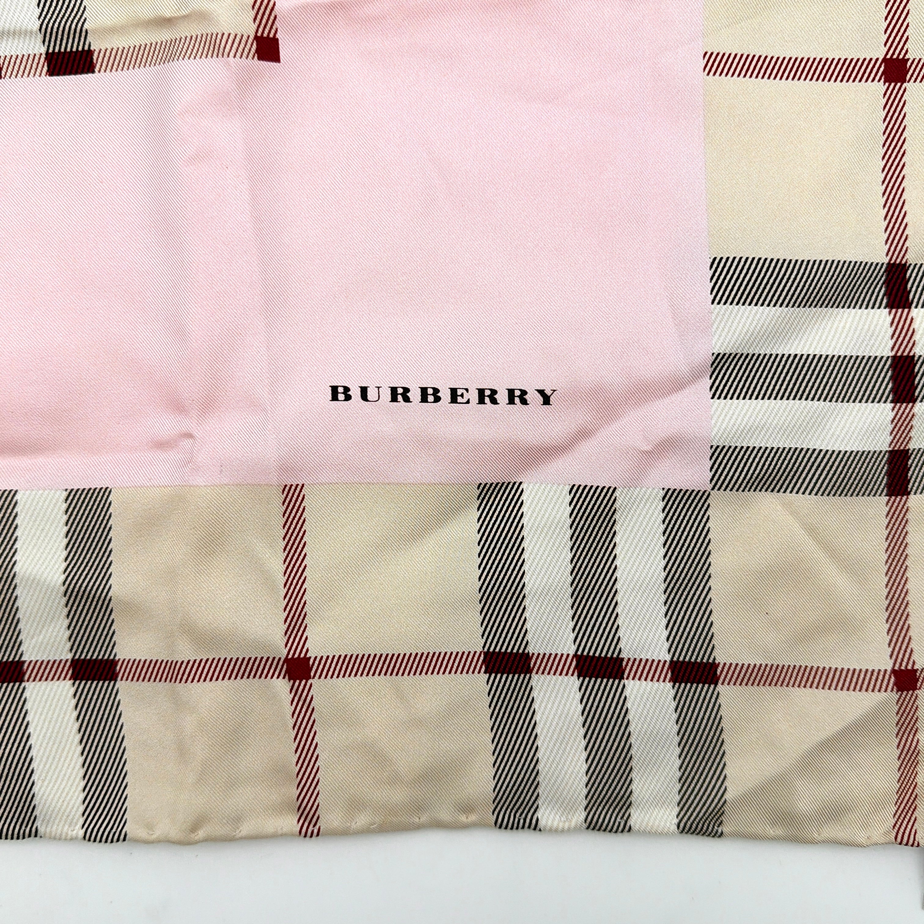 Burberry silk scarf in pale pink and beige, showcasing the iconic Nova Check pattern with burgundy highlights and a subtle brand signature.