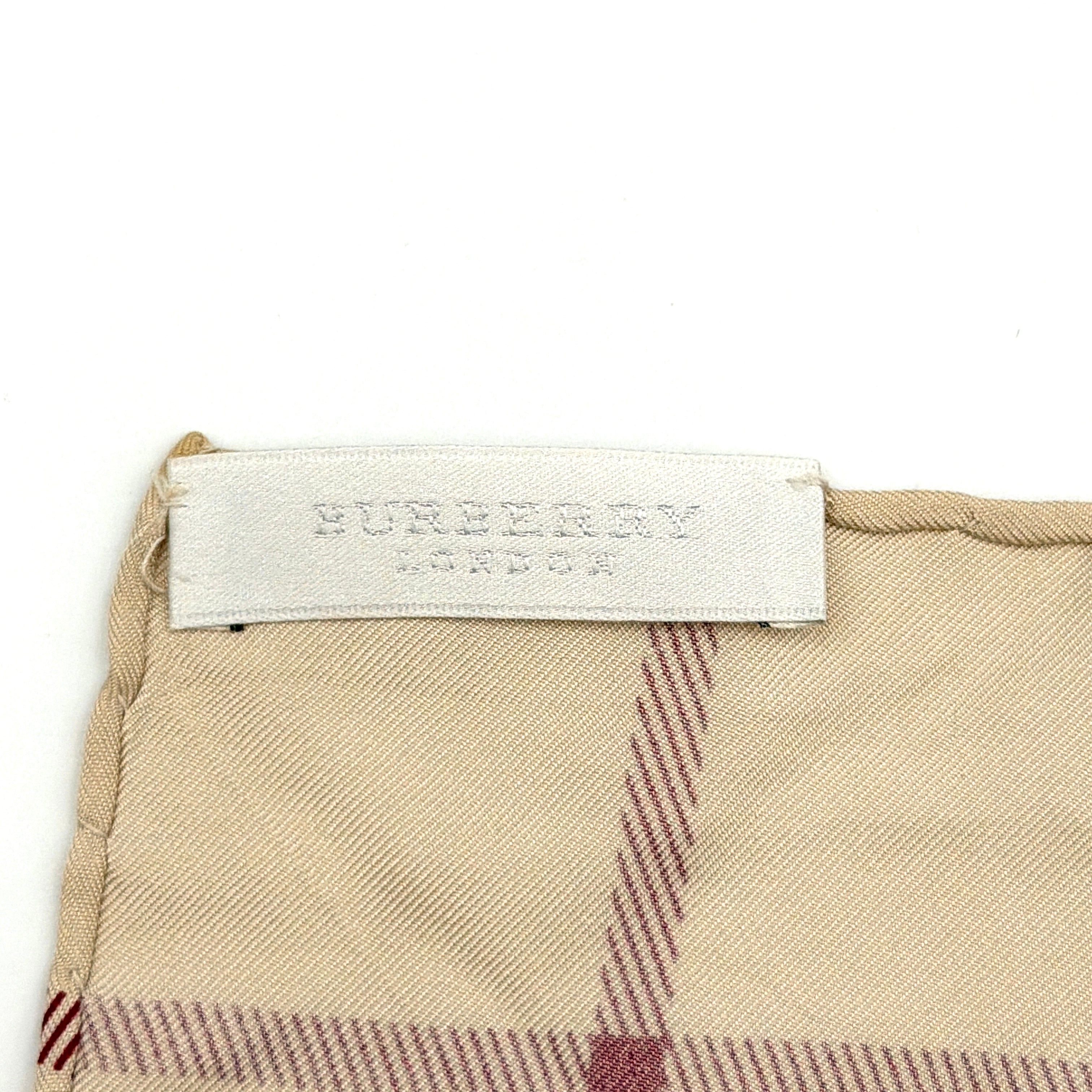 Burberry silk scarf in pale pink and beige, showcasing the iconic Nova Check pattern with burgundy highlights and a subtle brand signature.