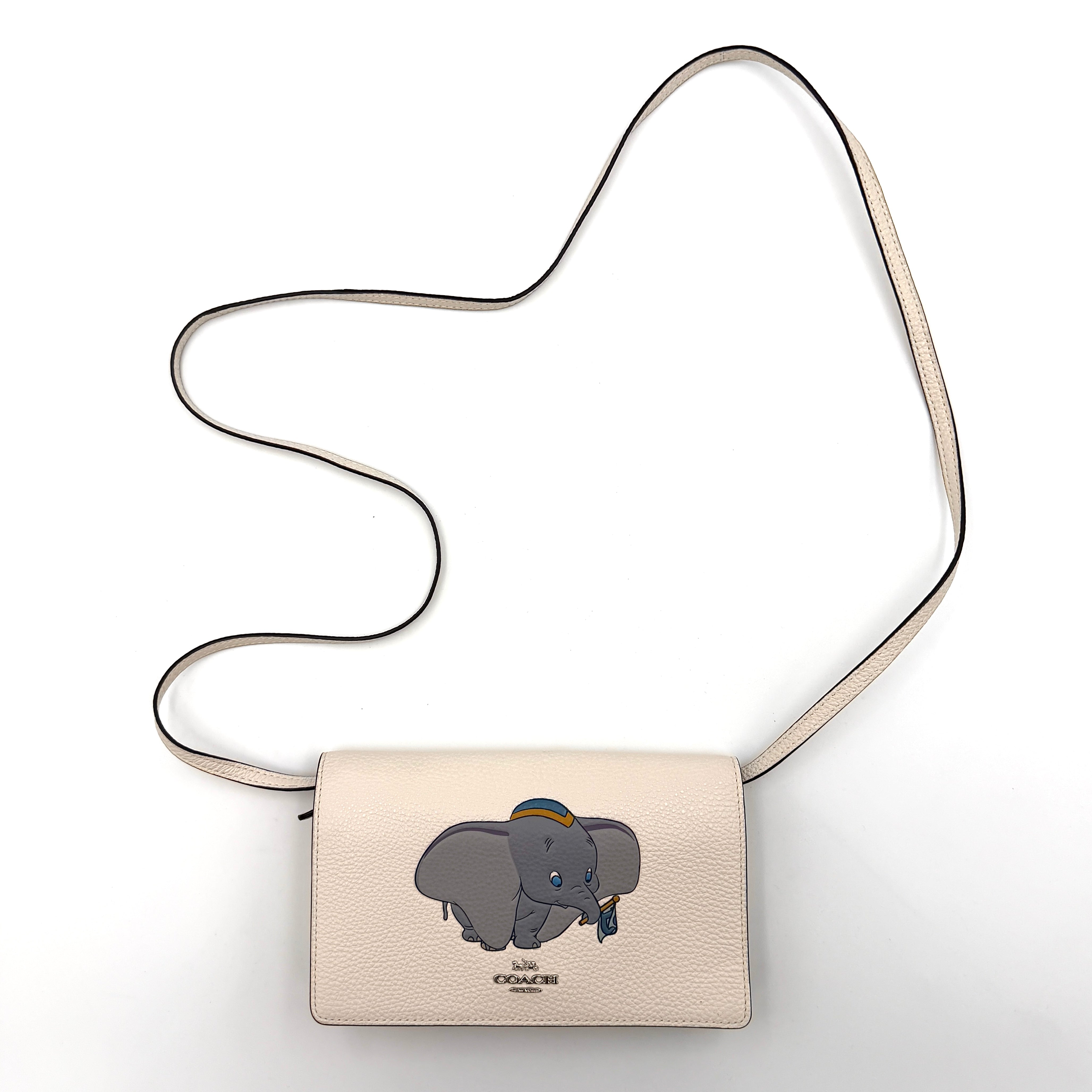 Coach x Disney Dumbo cream foldover crossbody bag with Dumbo illustration and slender strap, displayed against white background.