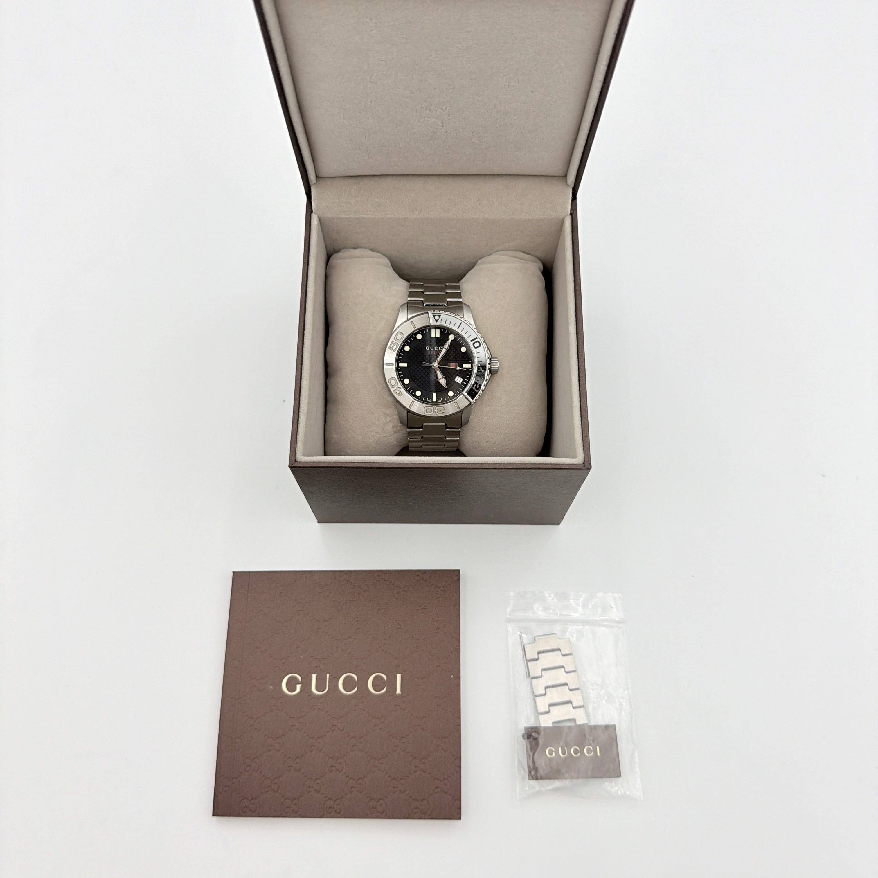 Gucci G-Timeless Sport Watch in silver with black dial, presented in its original box with booklet and extra links.