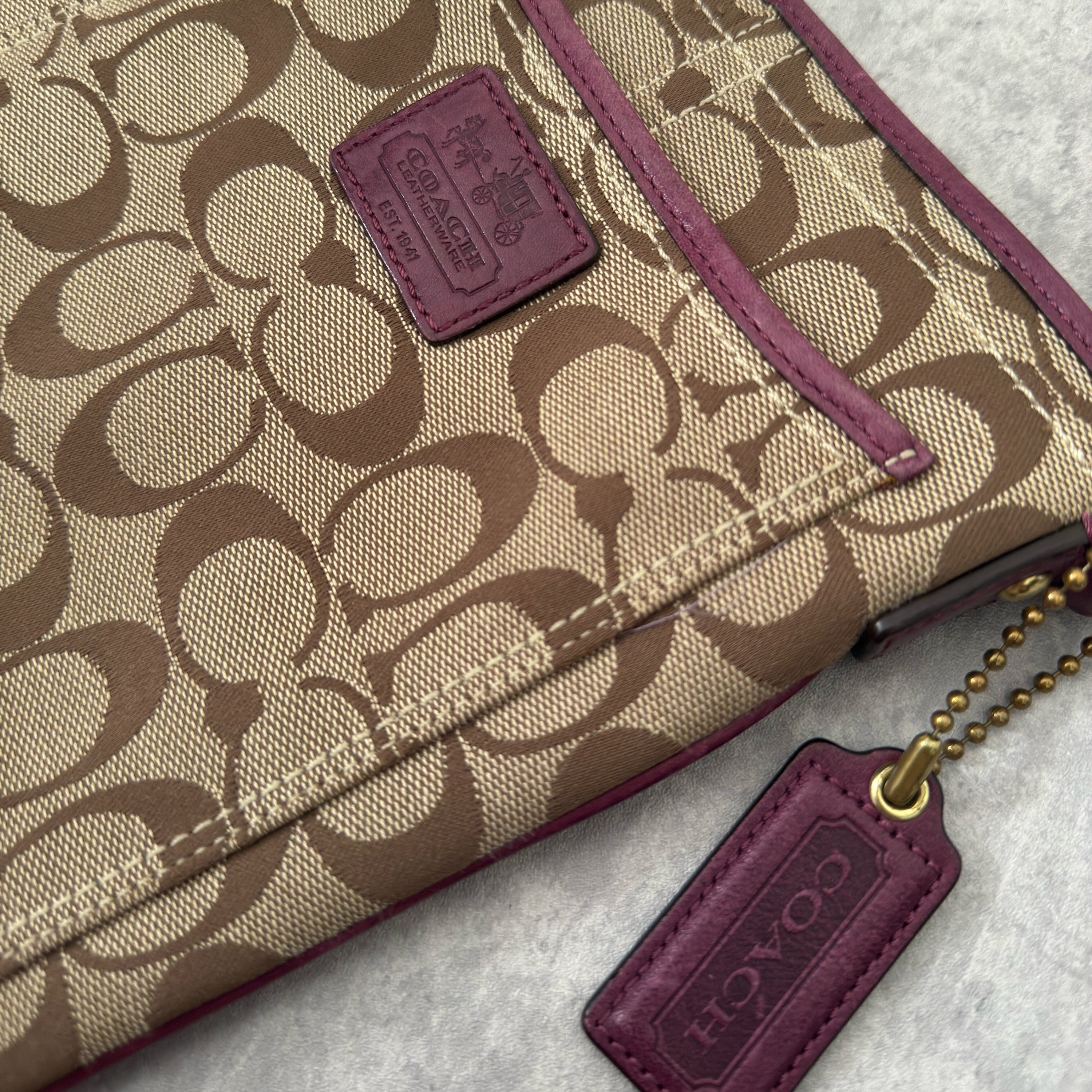 Coach Khaki Signature Crossbody Swing-pack in beige monogram canvas with purple leather trim, featuring an adjustable fabric strap and zippered top closure.