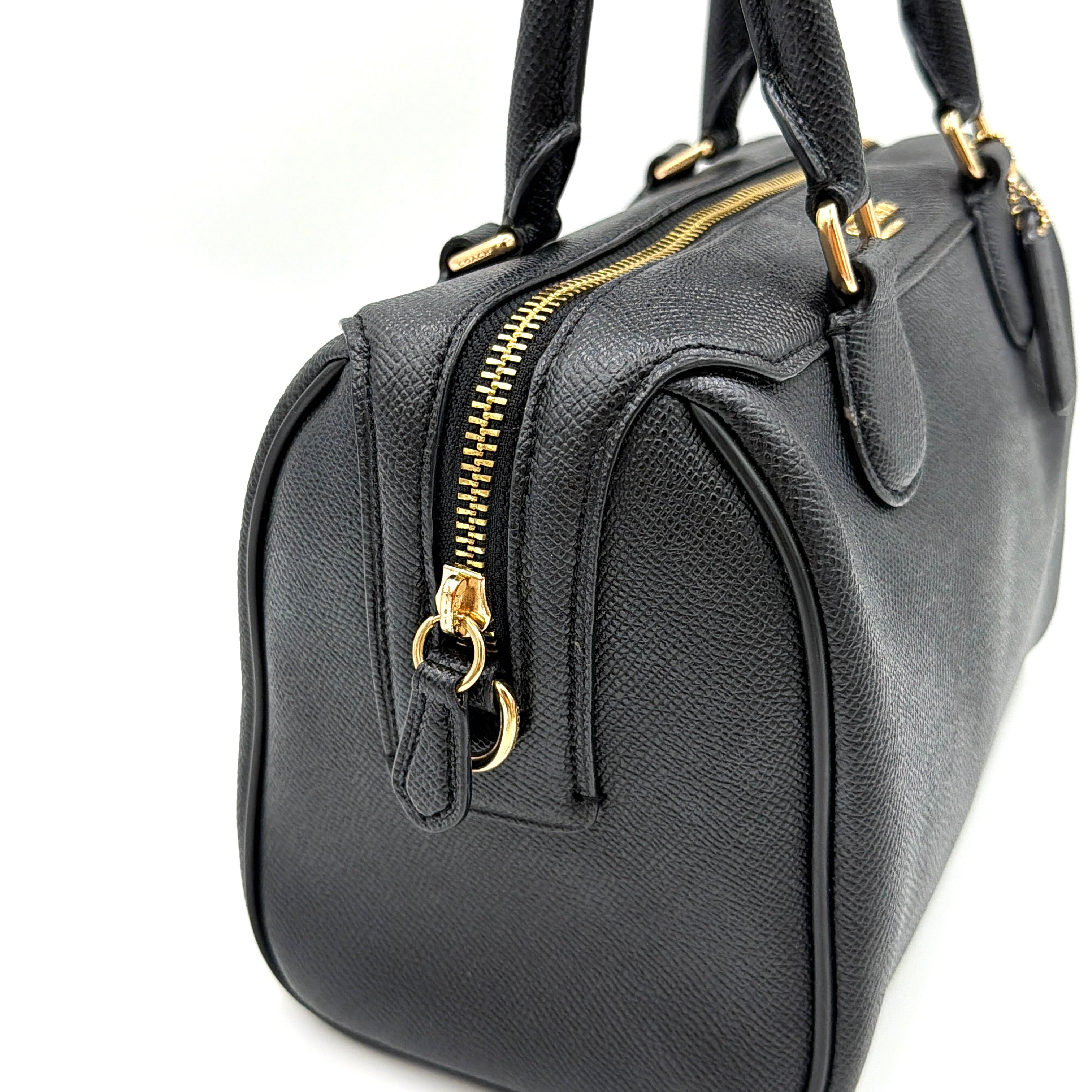 Coach Mini Bennett Boston Bag in black pebbled leather with gold hardware and detachable strap, styled against a clean backdrop.