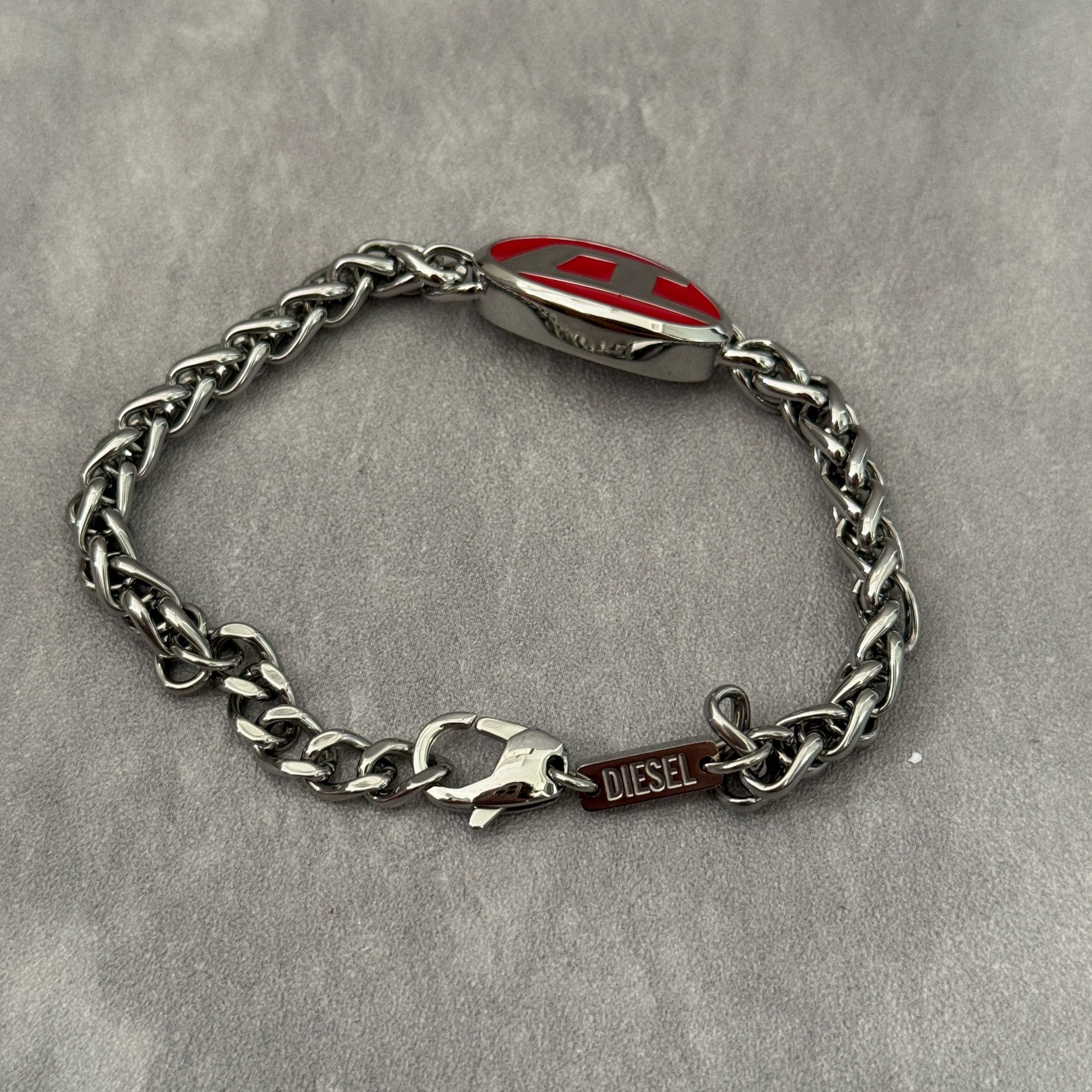 Diesel red lacquer and stainless steel chain bracelet with bold logo centerpiece and lobster clasp closure.