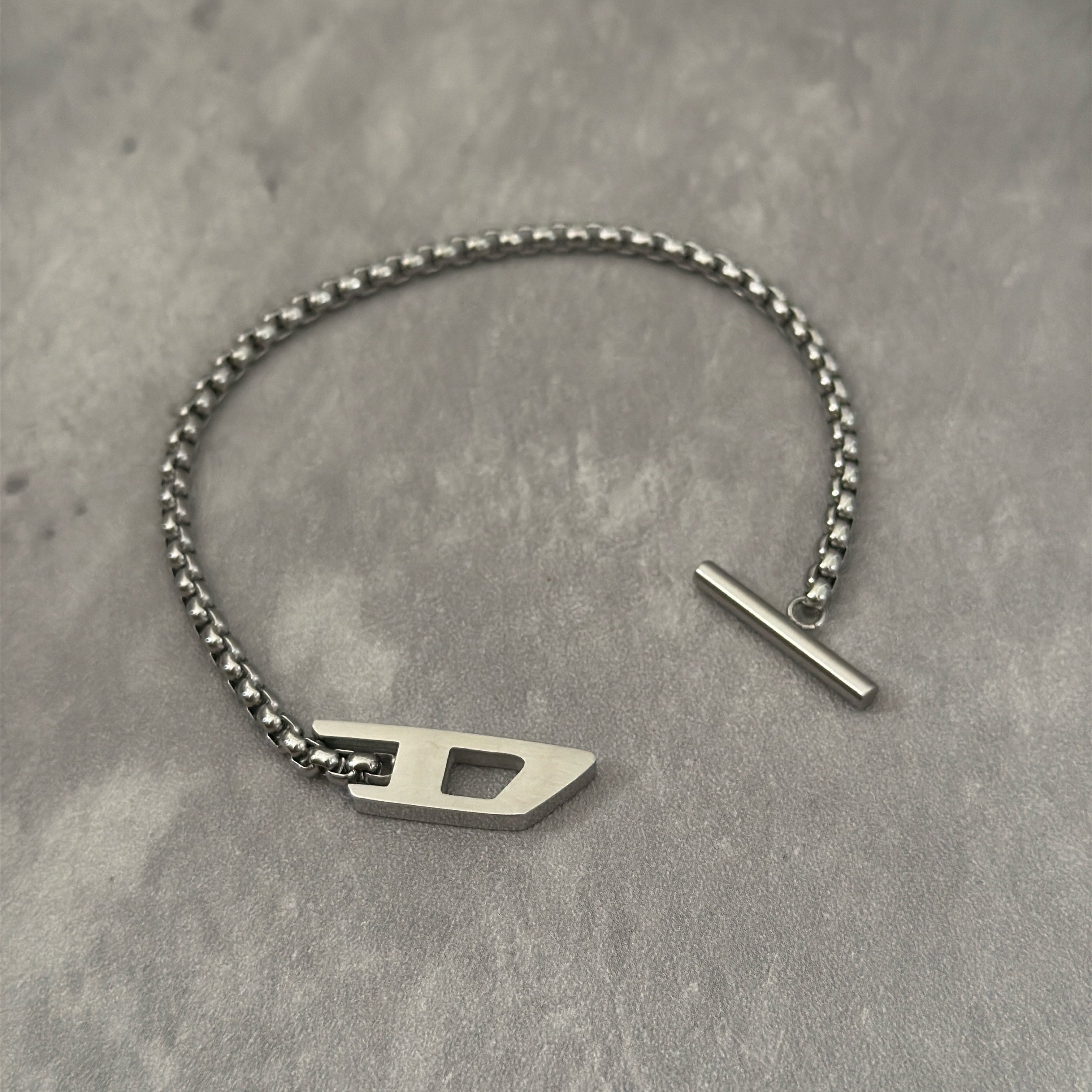 Diesel Signature D-Logo Stainless Steel Bracelet, featuring a silver-tone chain-link design with a bold Diesel "D" logo and a T-bar closure.