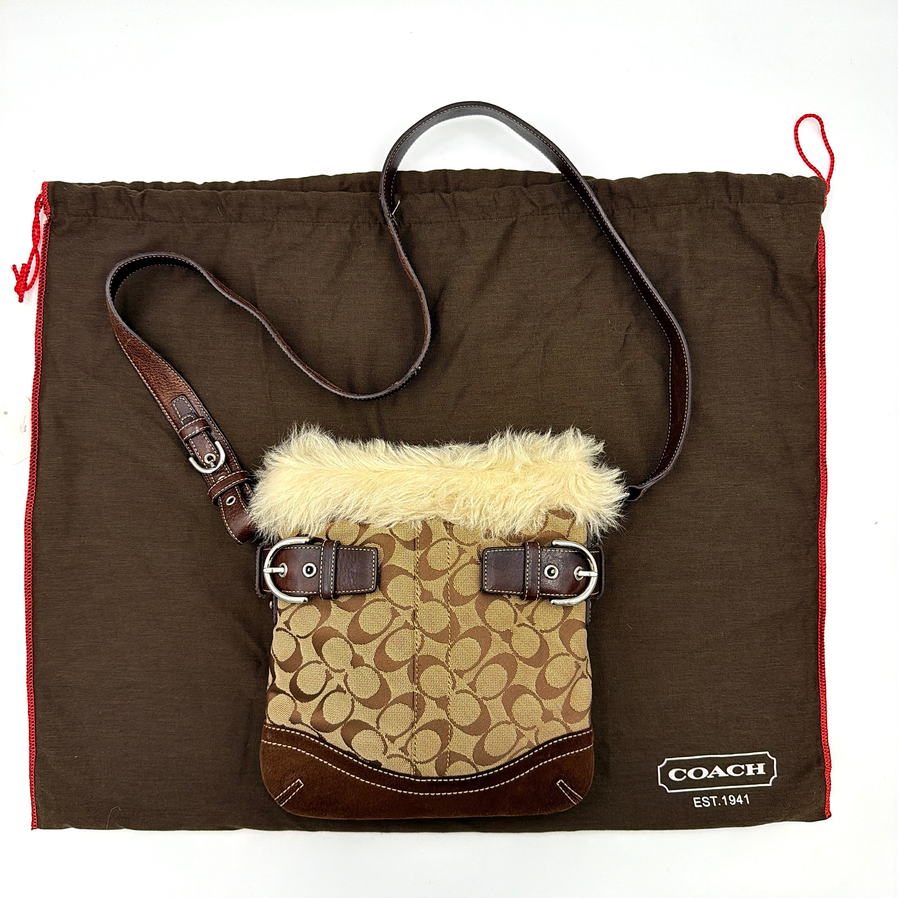 Coach Signature canvas crossbody bag in brown and beige with cream faux fur trim and leather buckle accents, shown with adjustable strap.