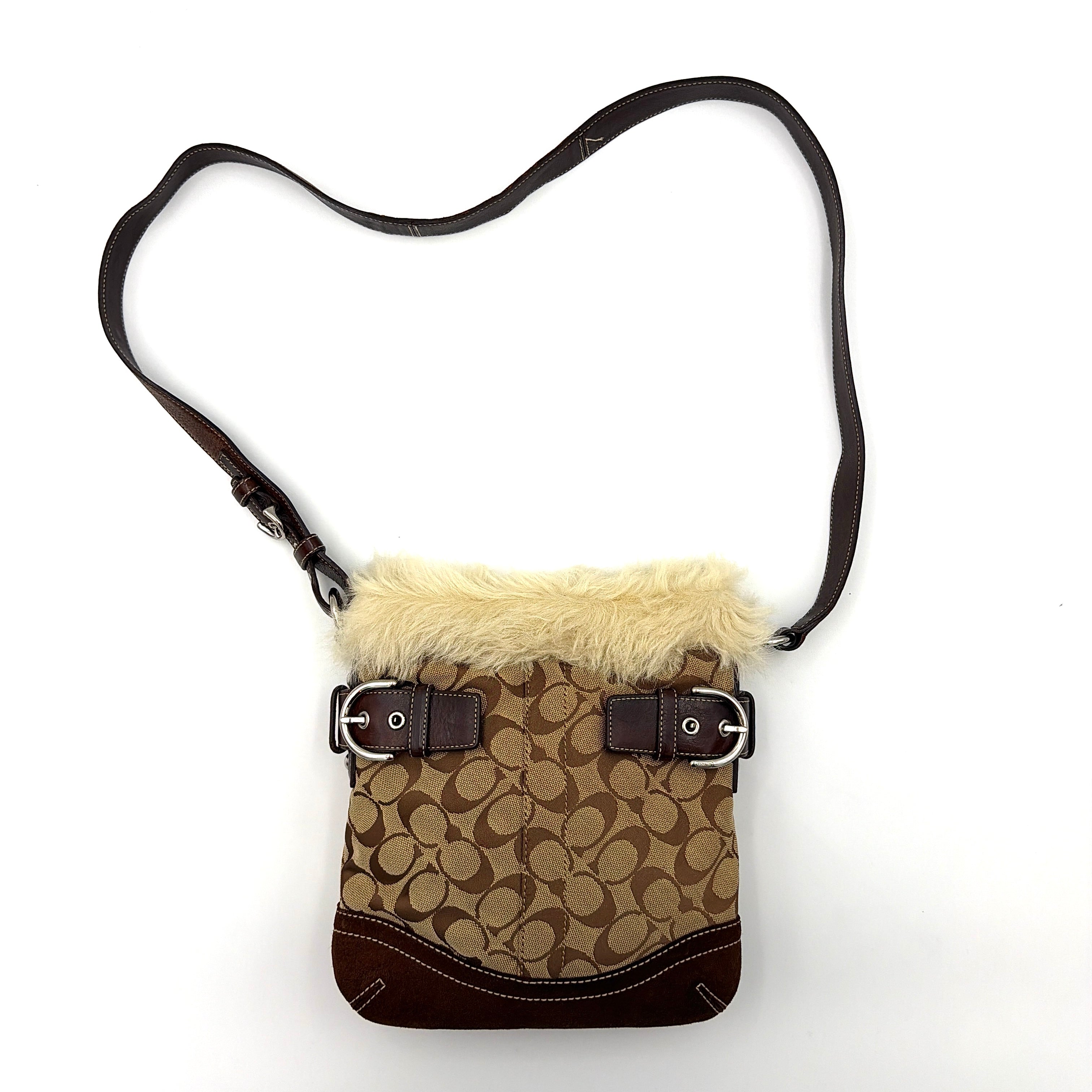 Coach Signature canvas crossbody bag in brown and beige with cream faux fur trim and leather buckle accents, shown with adjustable strap.