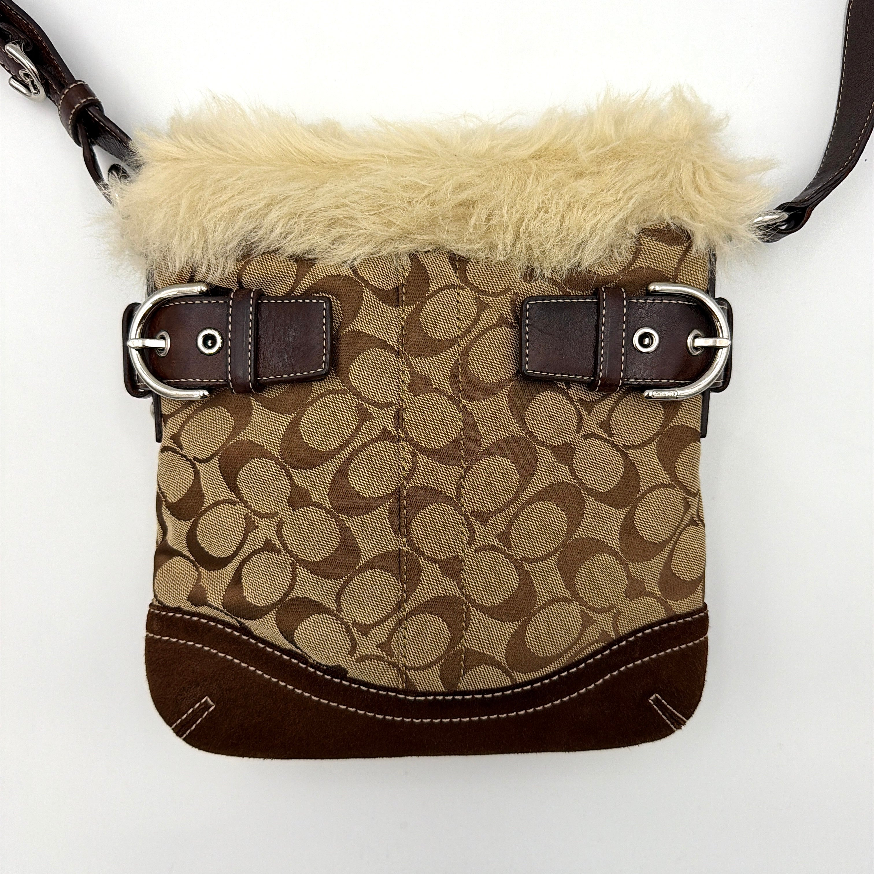 Coach Signature canvas crossbody bag in brown and beige with cream faux fur trim and leather buckle accents, shown with adjustable strap.