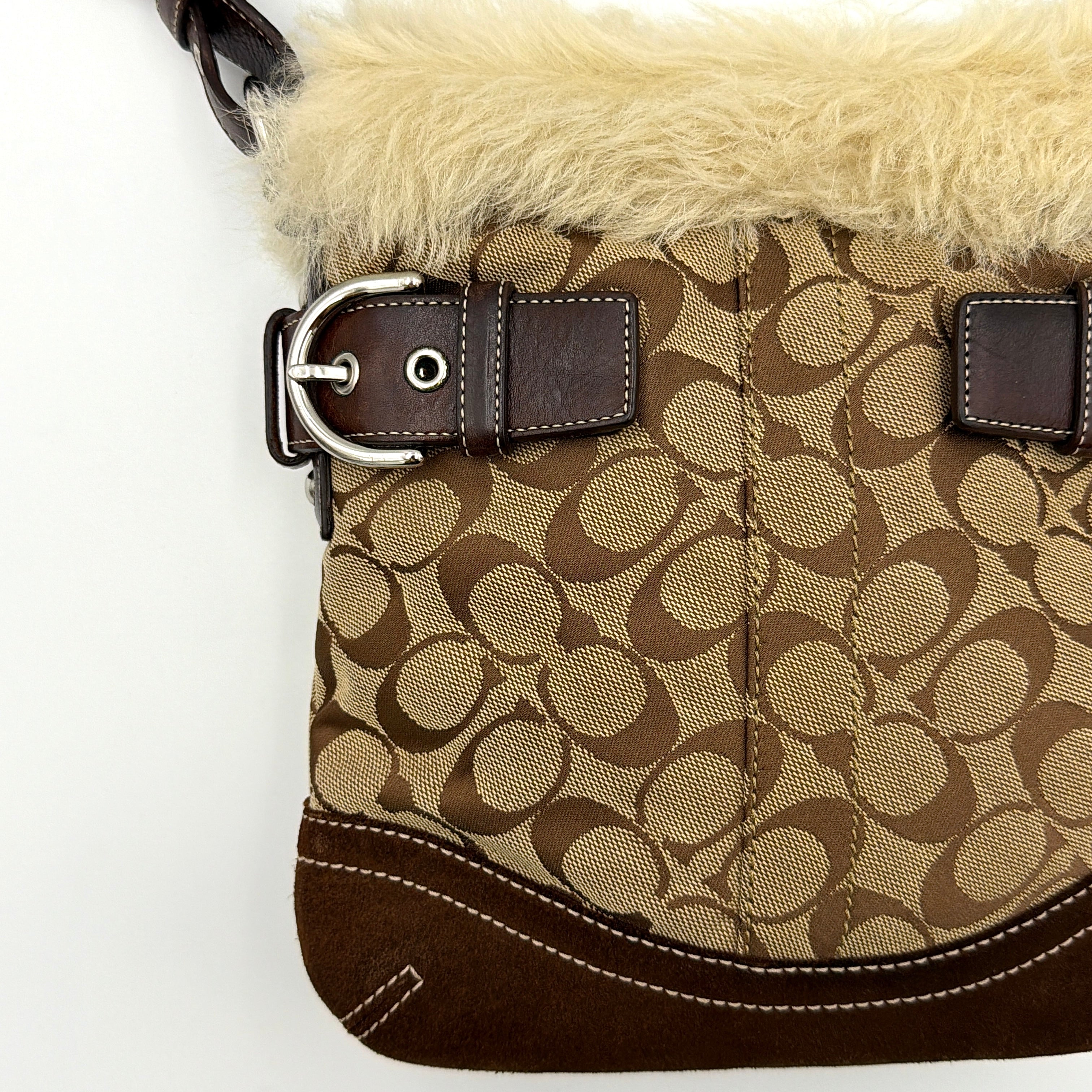 Coach Signature canvas crossbody bag in brown and beige with cream faux fur trim and leather buckle accents, shown with adjustable strap.
