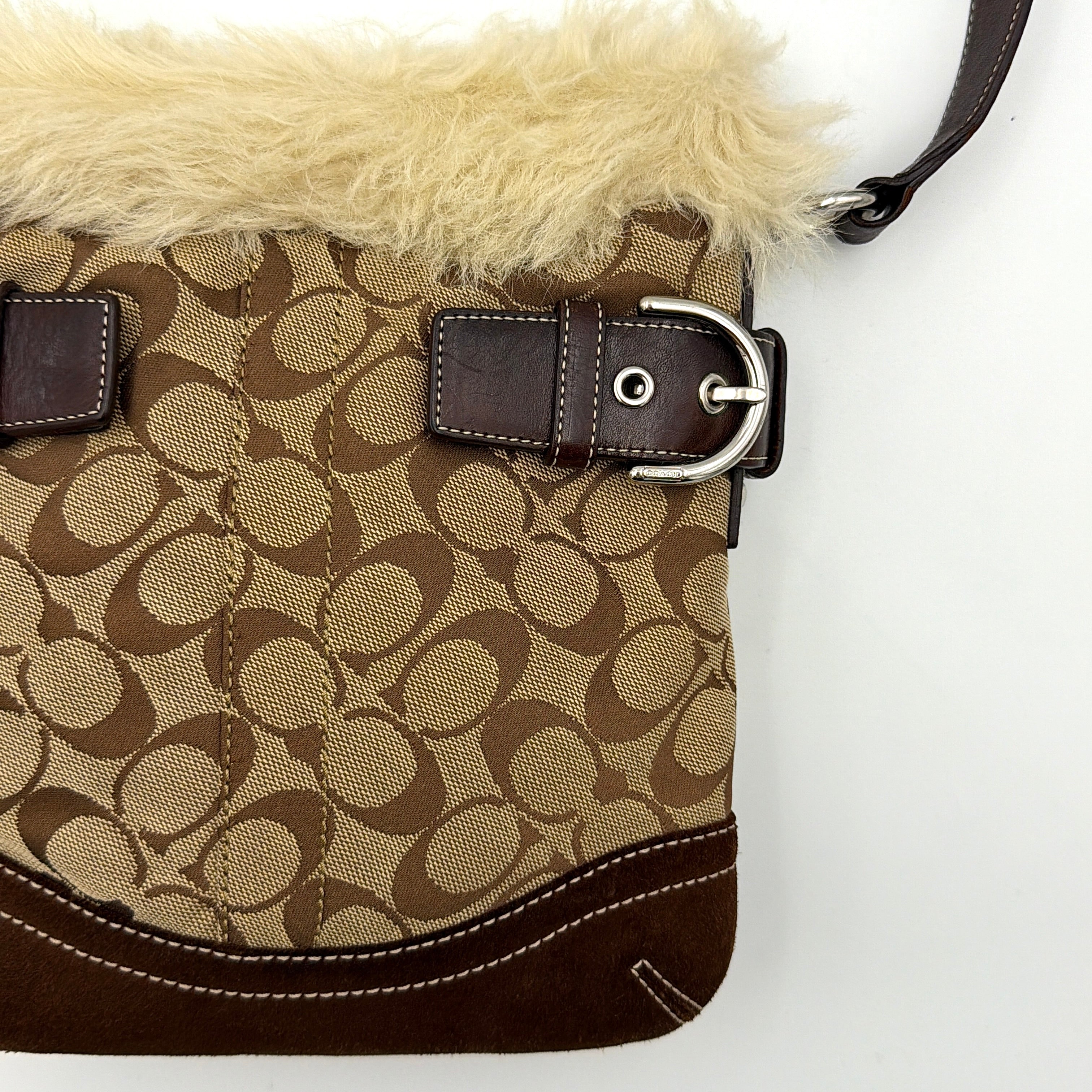 Coach Signature canvas crossbody bag in brown and beige with cream faux fur trim and leather buckle accents, shown with adjustable strap.