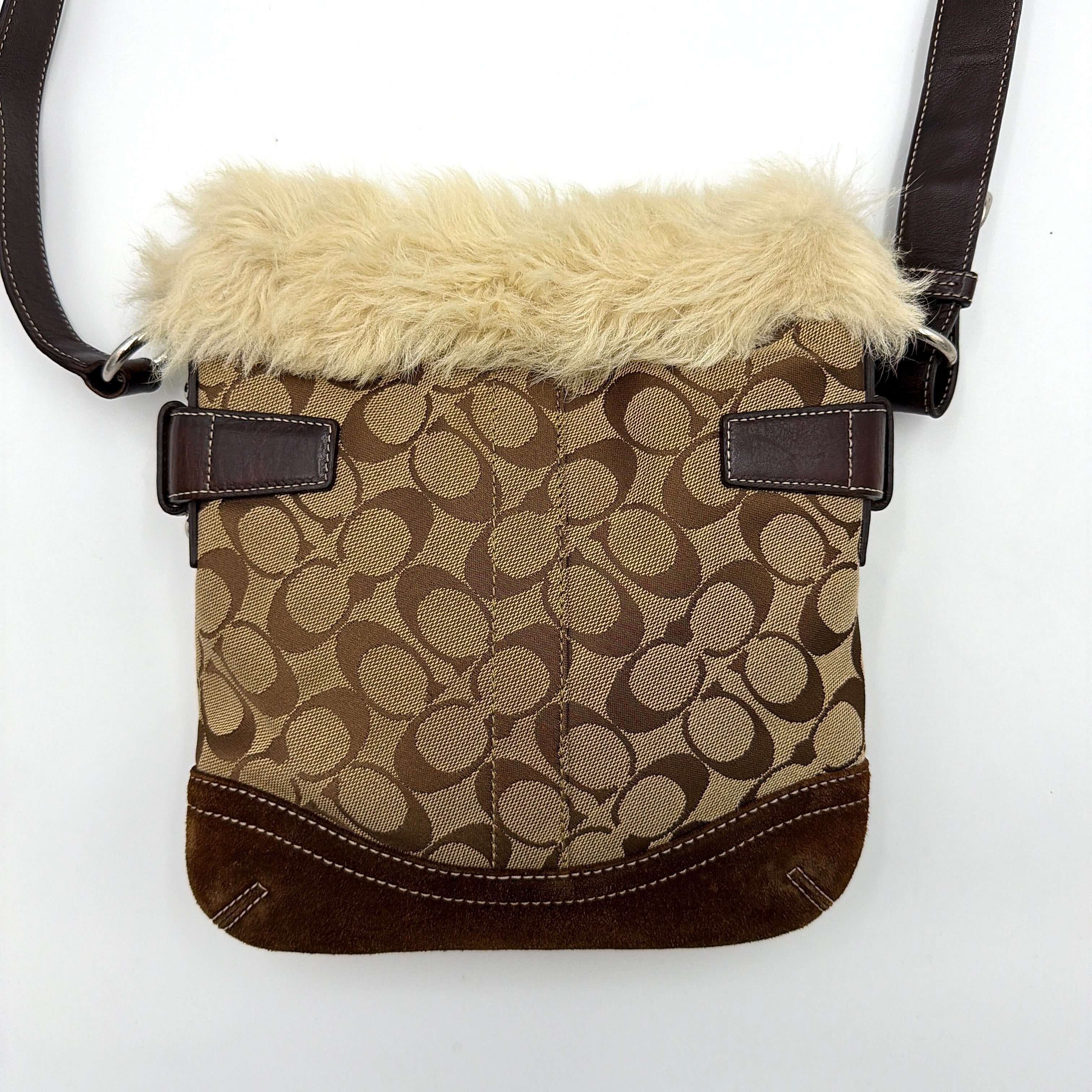 Coach Signature canvas crossbody bag in brown and beige with cream faux fur trim and leather buckle accents, shown with adjustable strap.