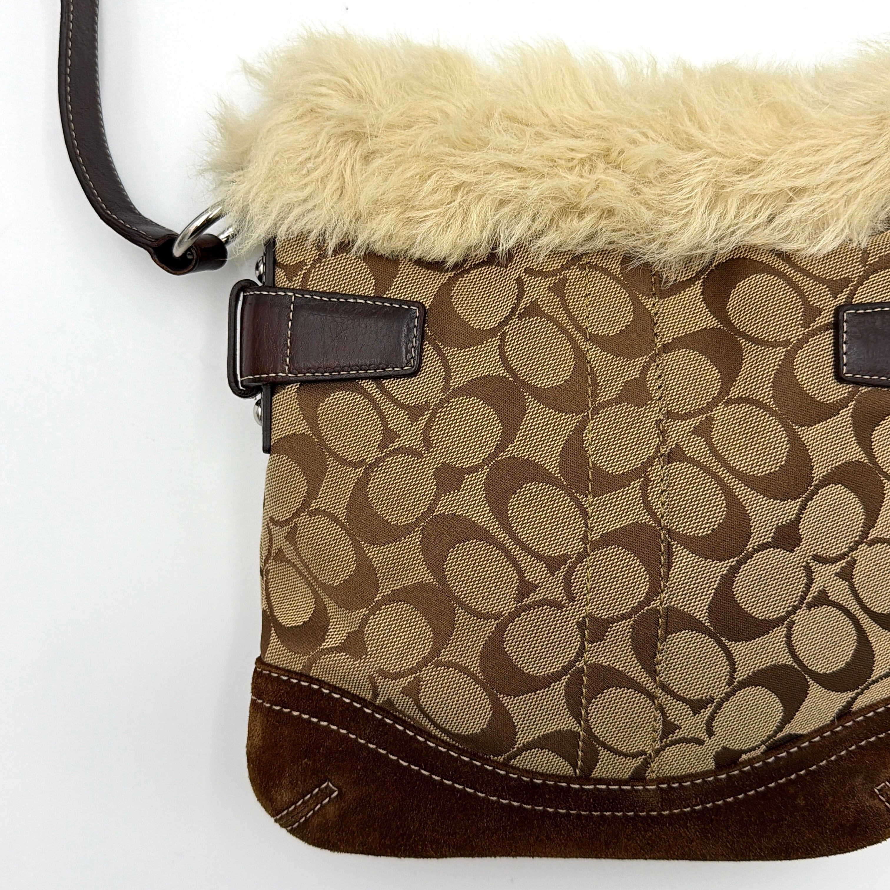 Coach Signature canvas crossbody bag in brown and beige with cream faux fur trim and leather buckle accents, shown with adjustable strap.