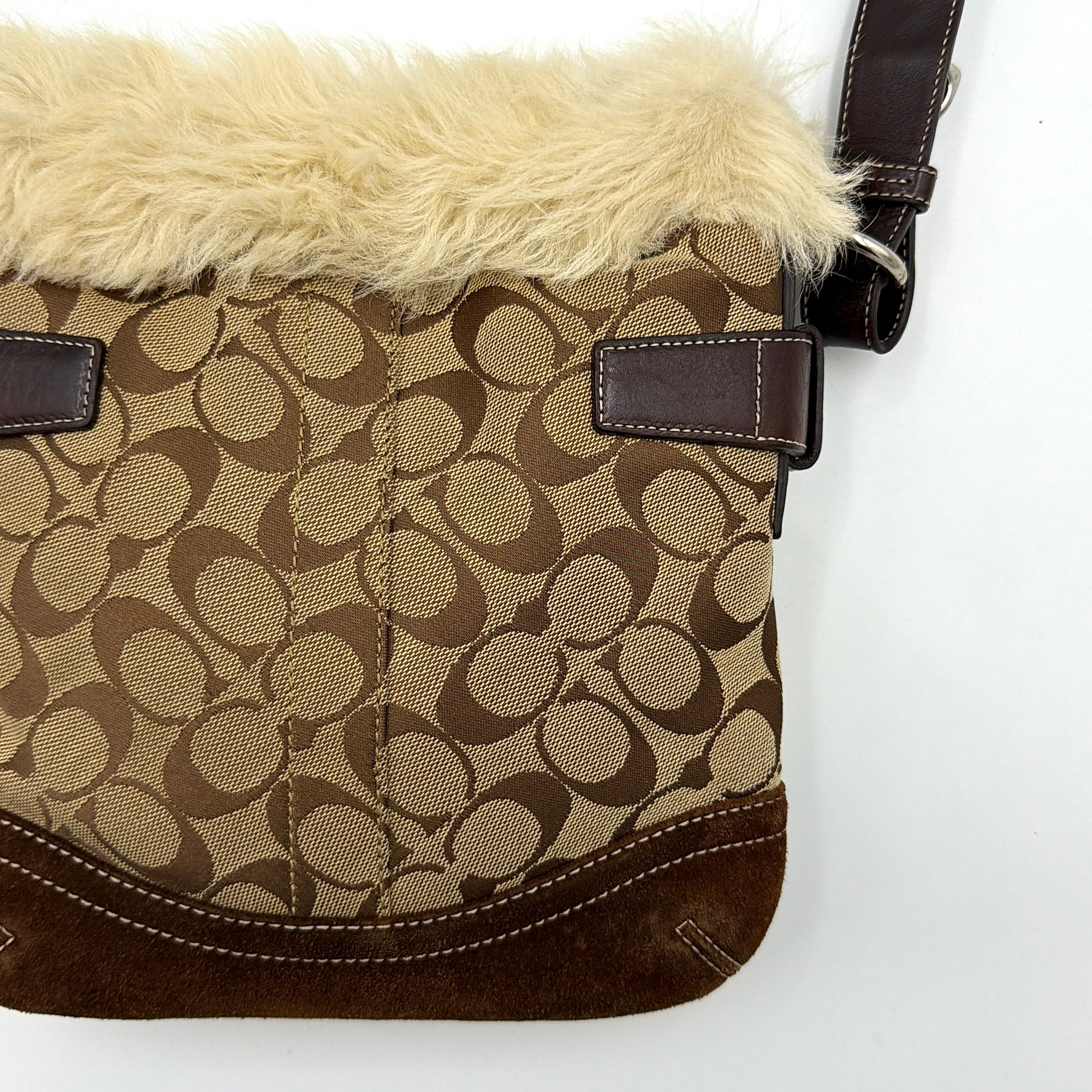 Coach Signature canvas crossbody bag in brown and beige with cream faux fur trim and leather buckle accents, shown with adjustable strap.