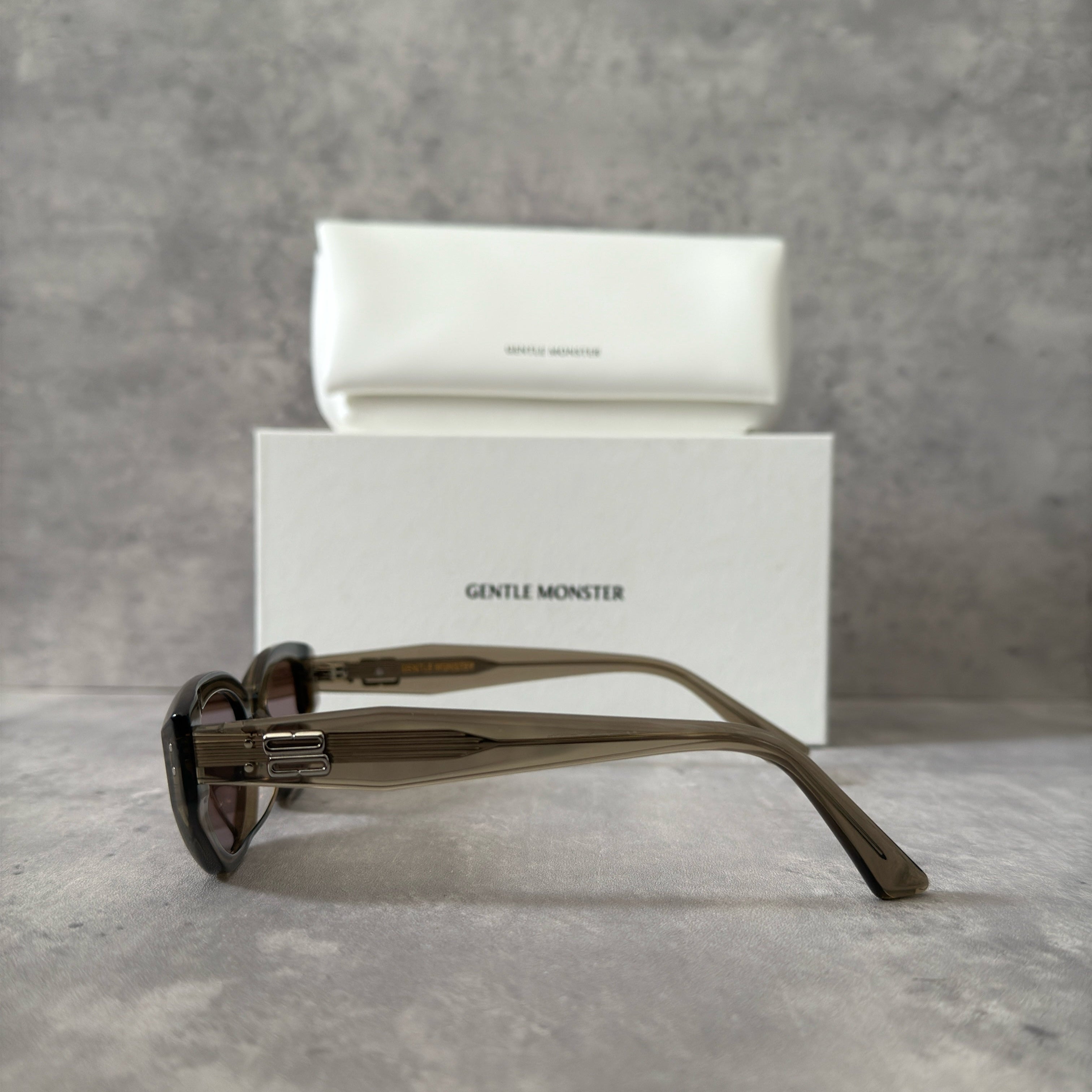 Gentle Monster ROCOCO KC6 sunglasses in translucent smoky brown acetate, featuring a bold sculpted design, tinted brown lenses, and signature metal temple detailing.