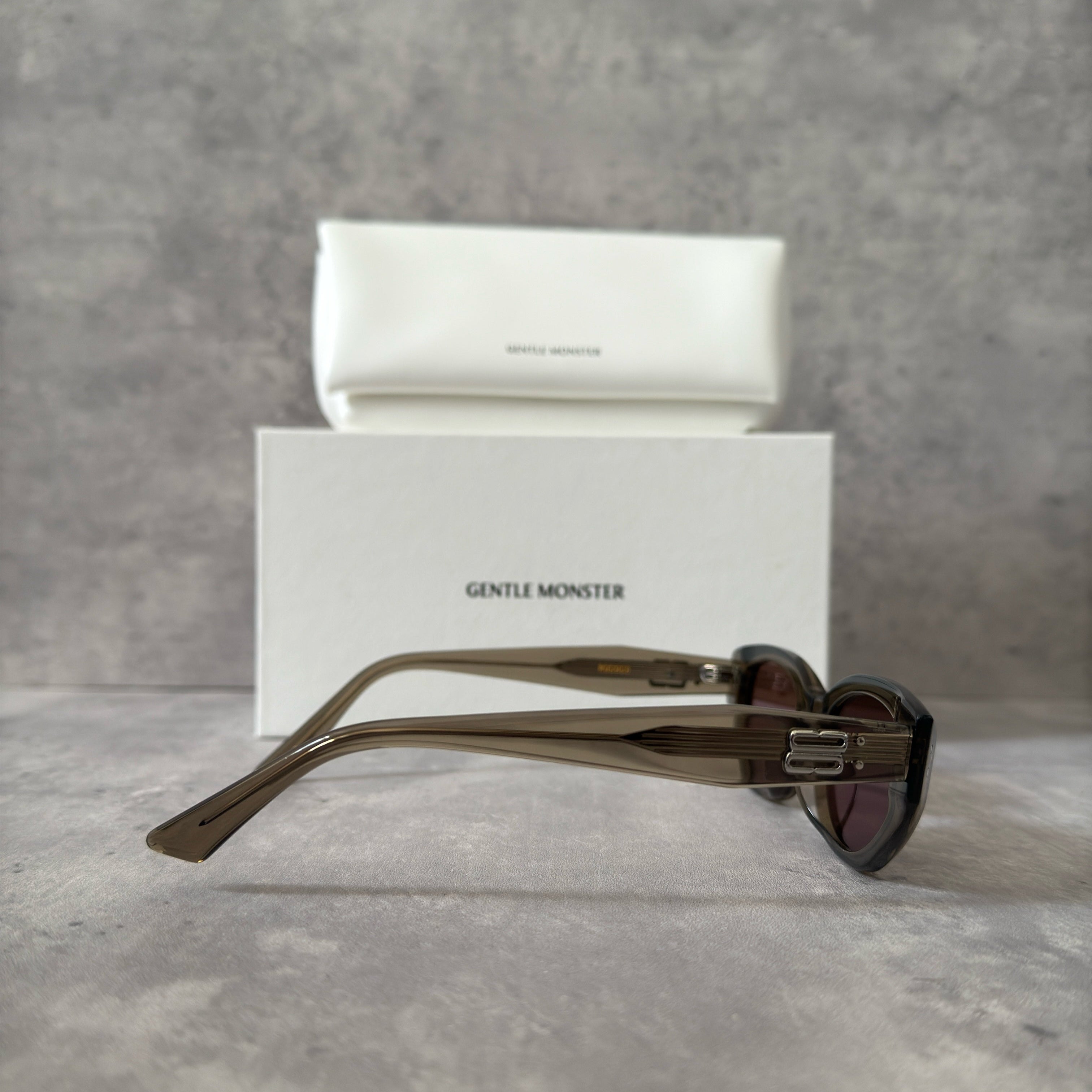 Gentle Monster ROCOCO KC6 sunglasses in translucent smoky brown acetate, featuring a bold sculpted design, tinted brown lenses, and signature metal temple detailing.