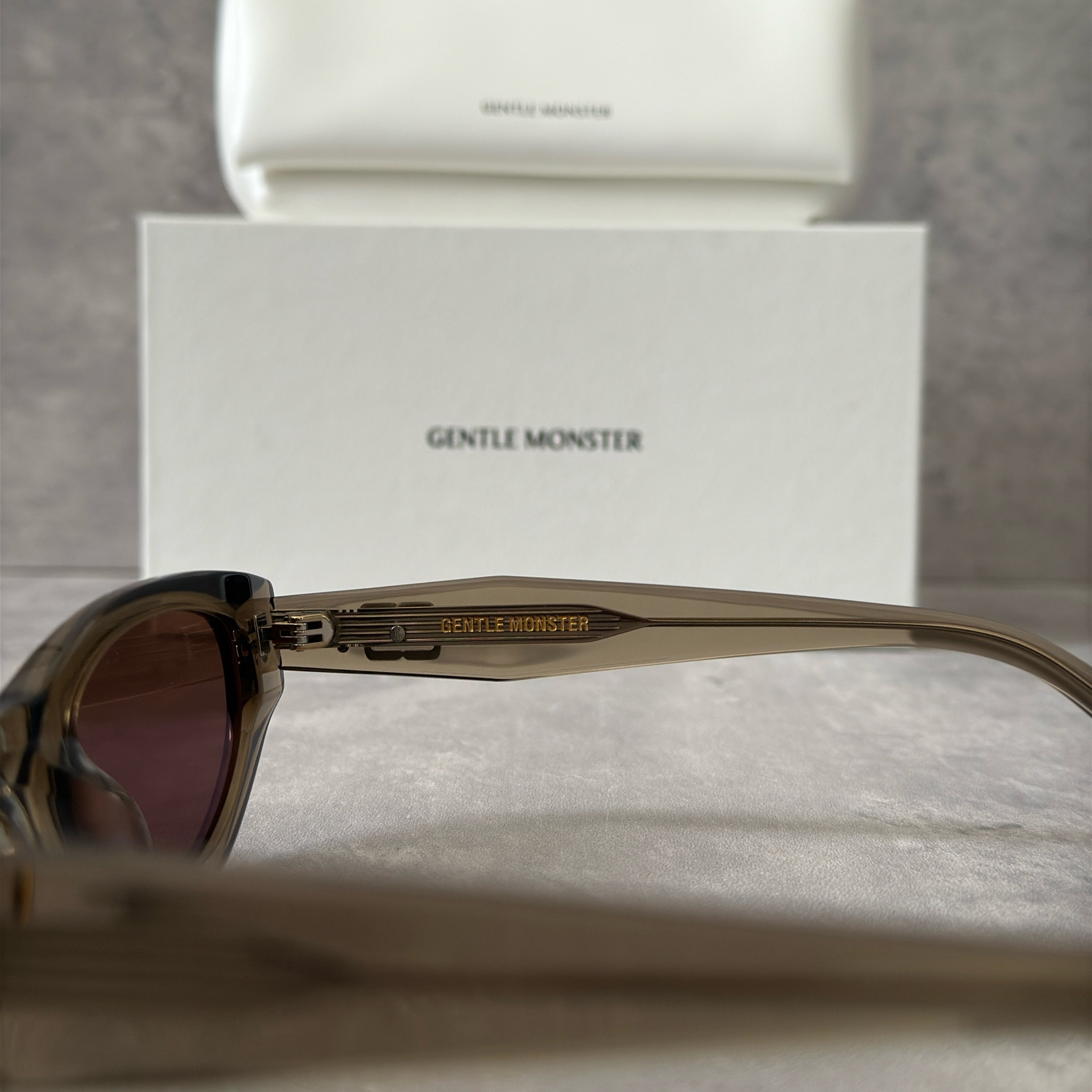 Gentle Monster ROCOCO KC6 sunglasses in translucent smoky brown acetate, featuring a bold sculpted design, tinted brown lenses, and signature metal temple detailing.