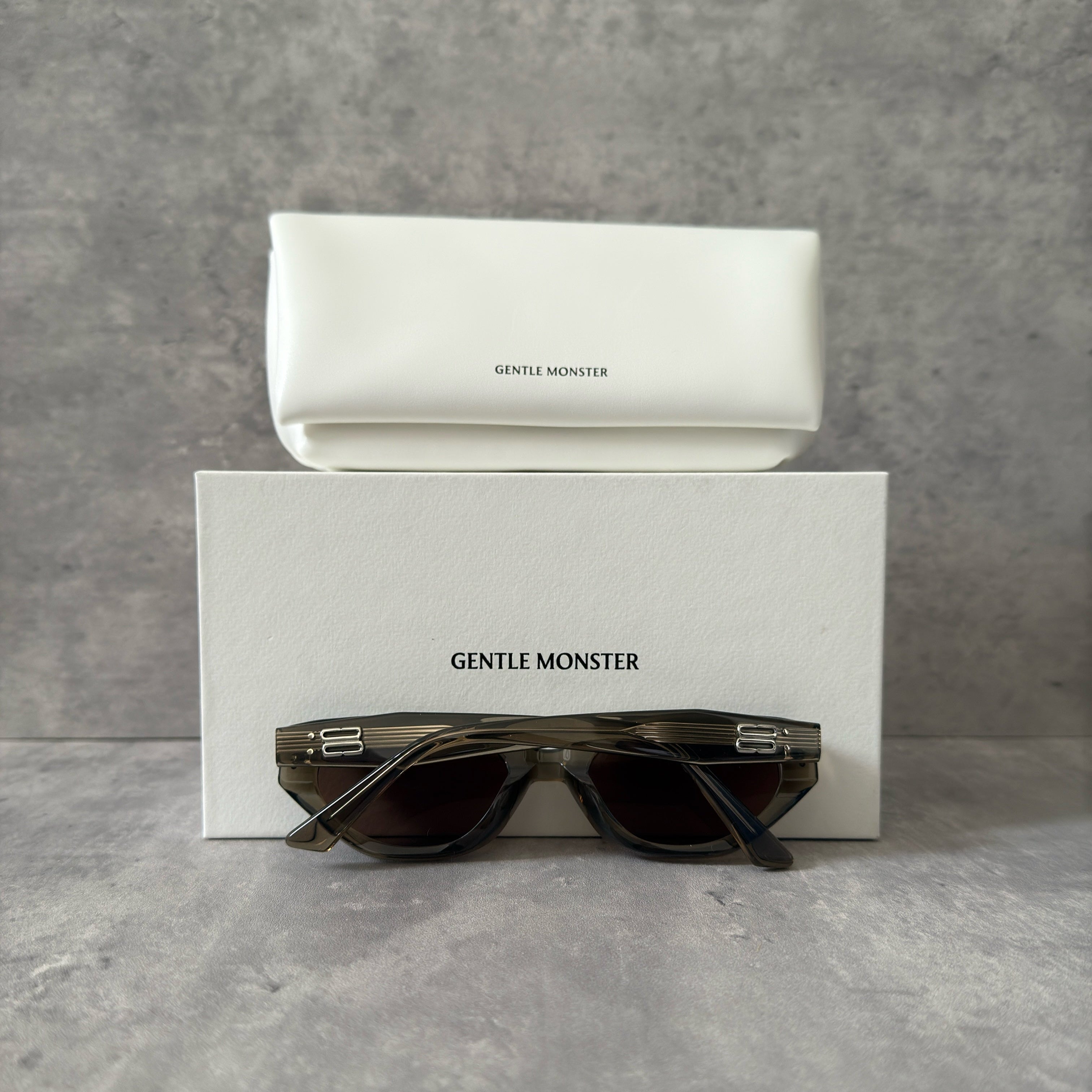 Gentle Monster ROCOCO KC6 sunglasses in translucent smoky brown acetate, featuring a bold sculpted design, tinted brown lenses, and signature metal temple detailing.